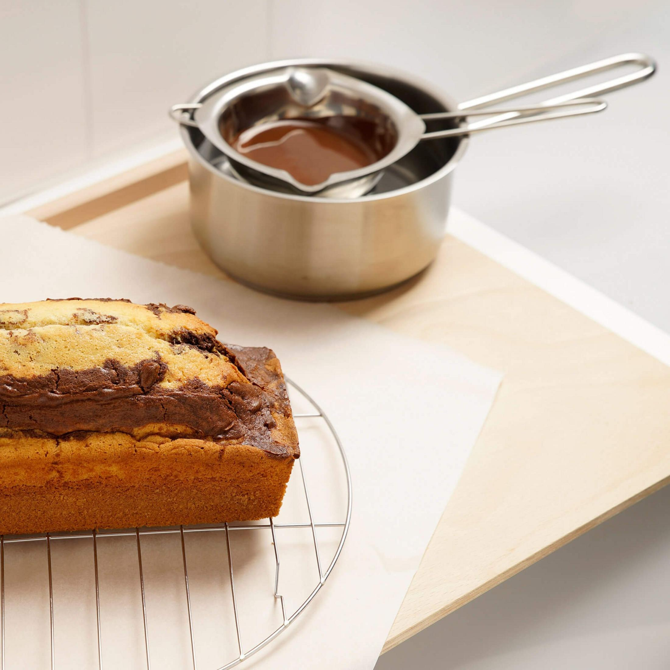 Marmorierter Kuchen auf einem Gitter mit Schmelzschale im Hintergrund.