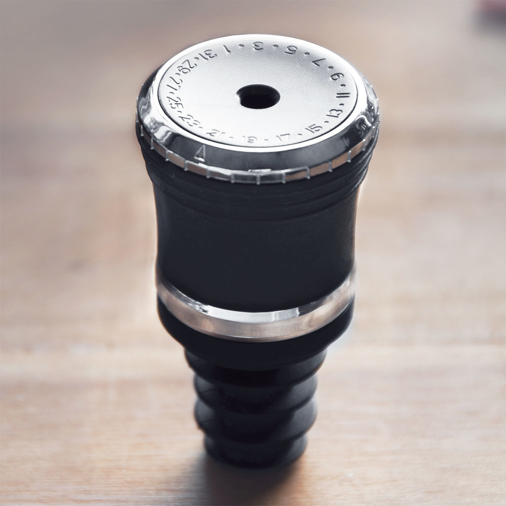 Tappo vino nero con anello argento e quadrante su sfondo legno.