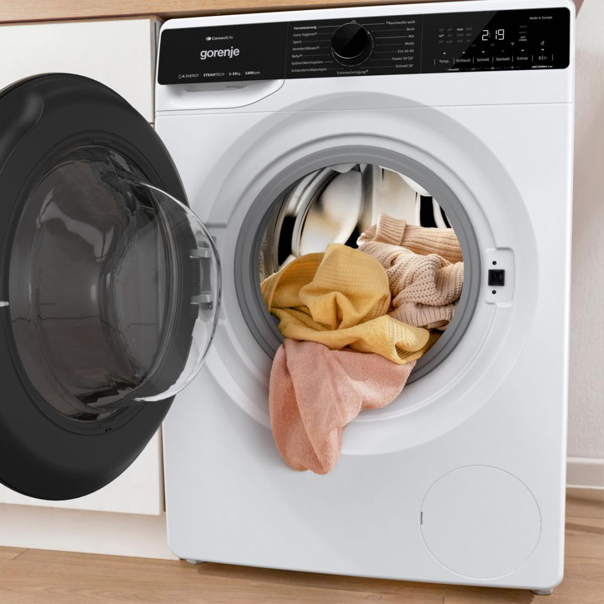 Eine weiße Gorenje Waschmaschine mit geöffneter Tür und bunter Wäsche.