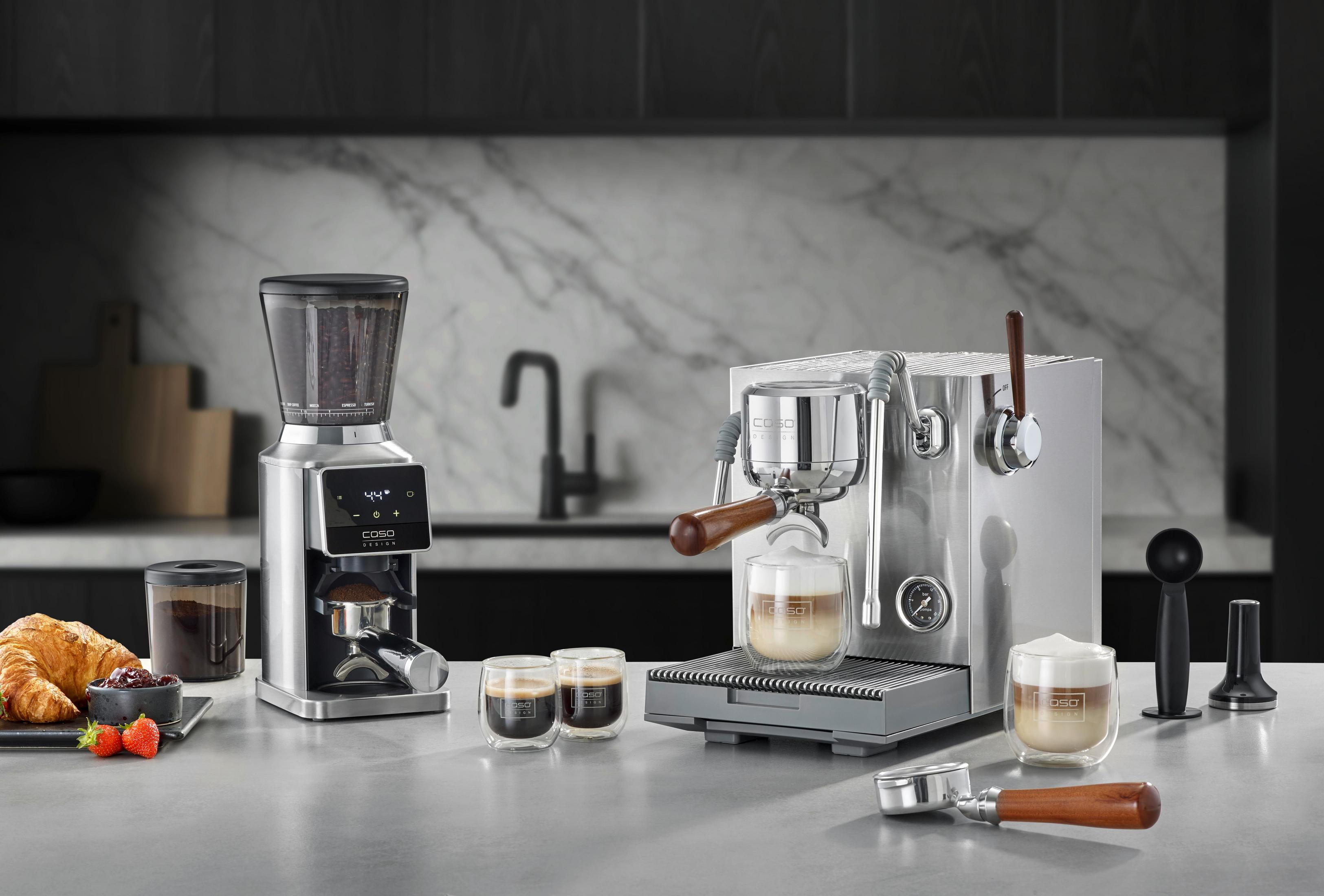 Kaffeemaschine mit Mühle, Croissant, Erdbeeren und Marmelade auf der Arbeitsplatte.