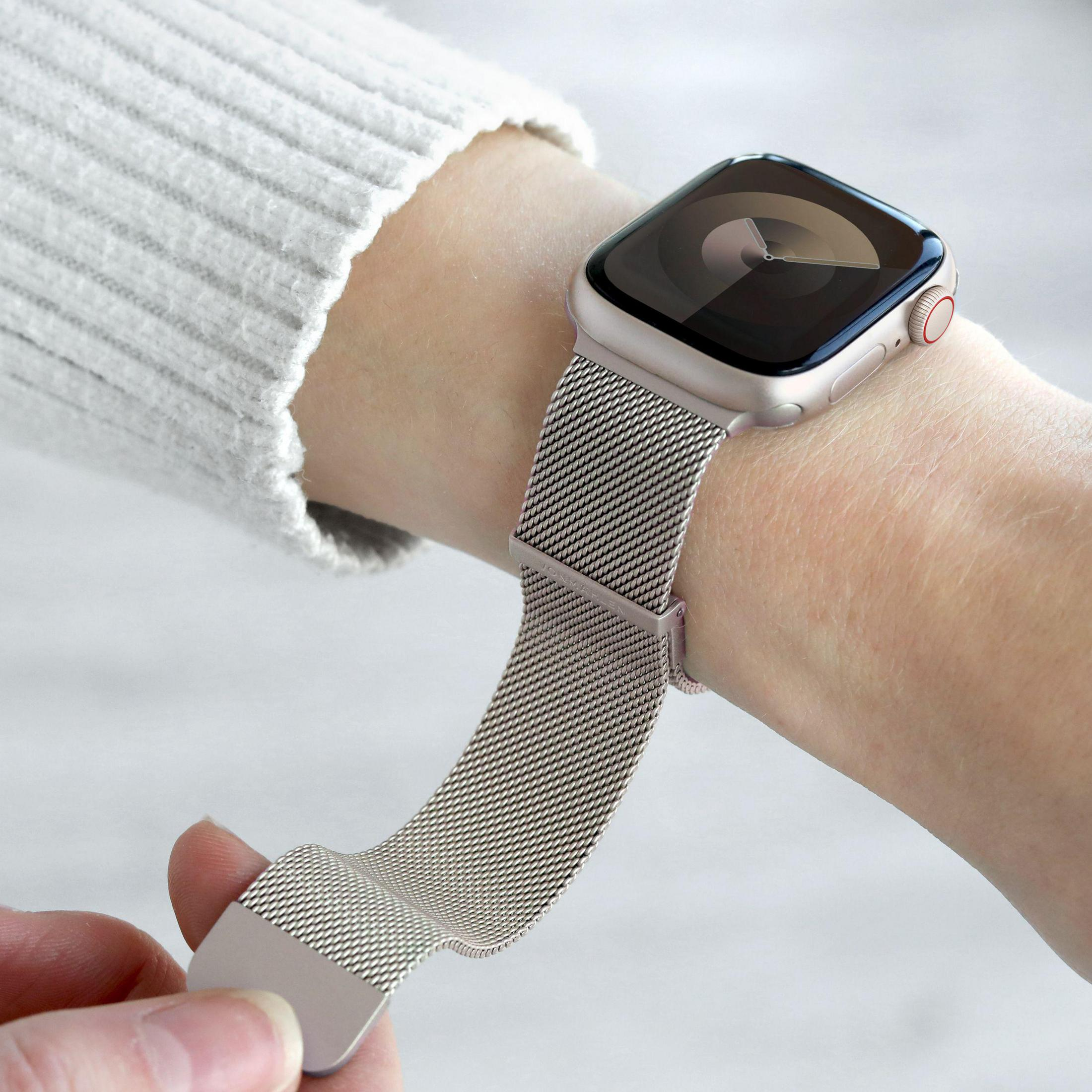 Une personne porte une montre connectée argentée avec bracelet Milanais au poignet.
