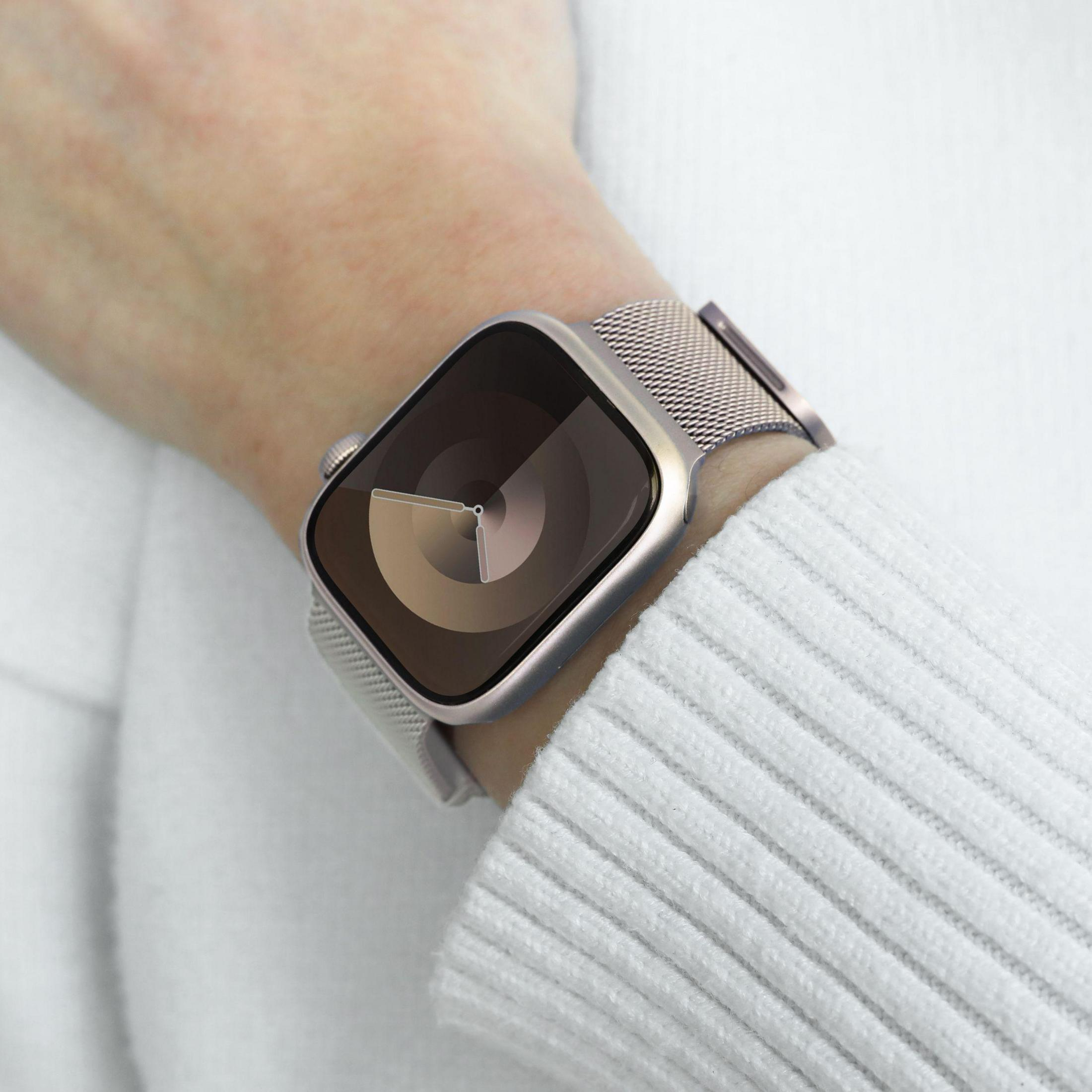 Poignet portant une Apple Watch argentée à bracelet milanais sur un pull blanc.