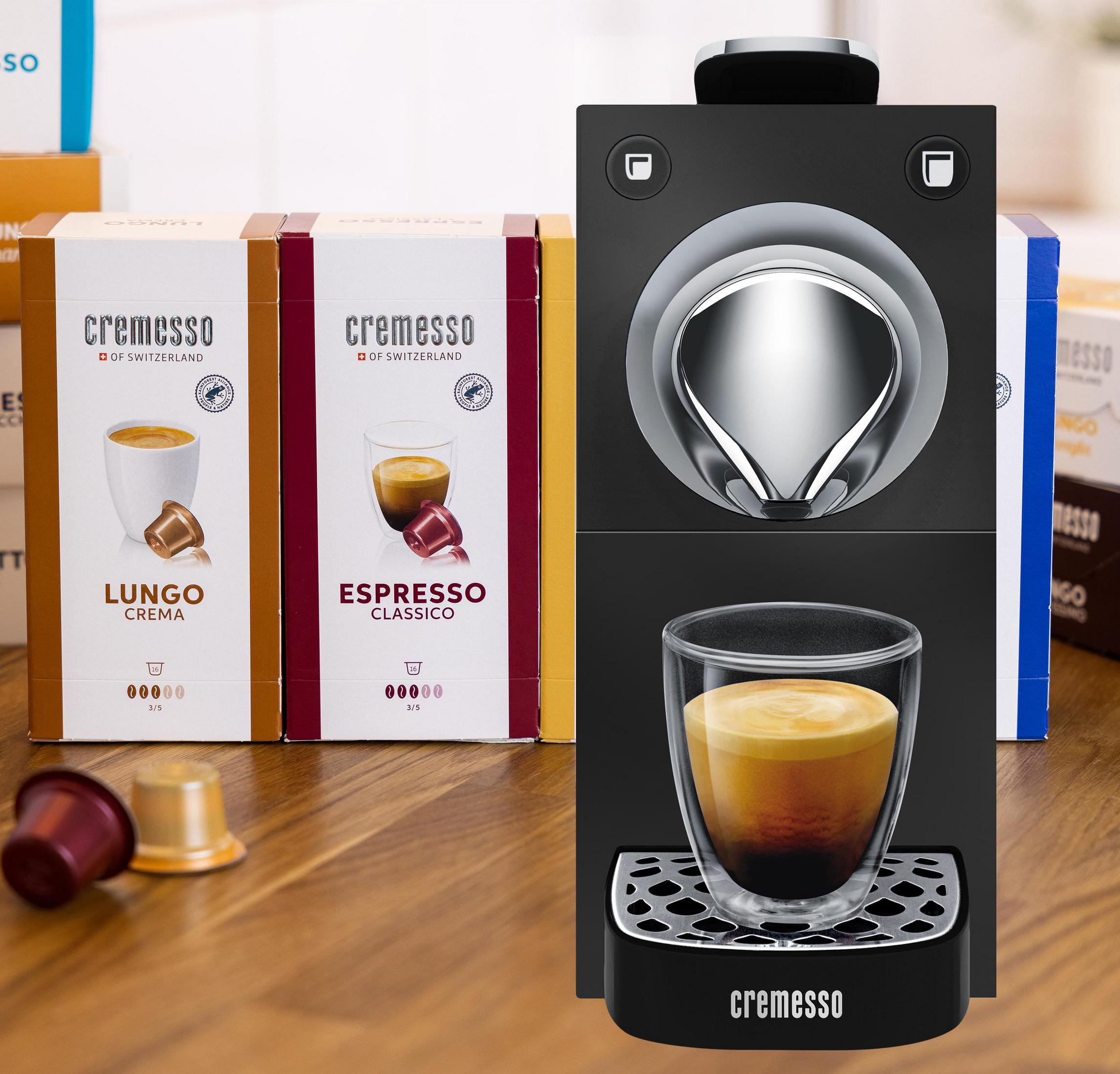 Crema Kaffeemaschine mit Kapseln und Packungen auf einem Holztisch.