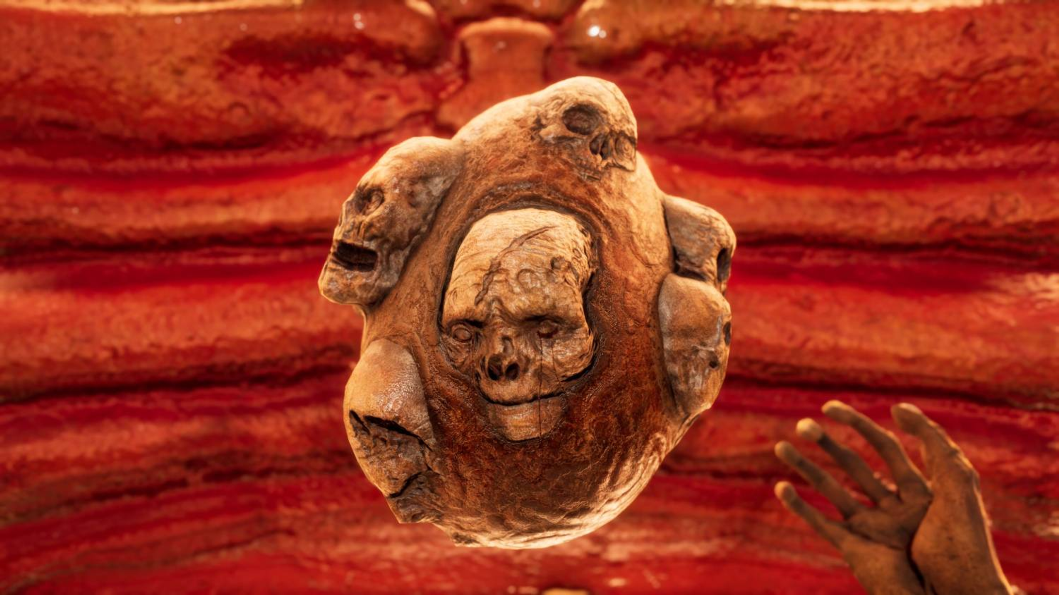 Una creatura con più volti e una mano su uno sfondo rosso stratificato.