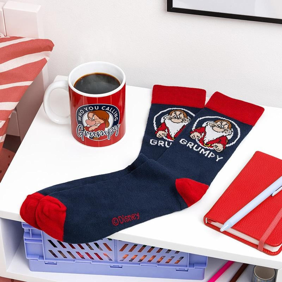 Una taza roja con Grumpy y un par de calcetines con Grumpy en un estante blanco.