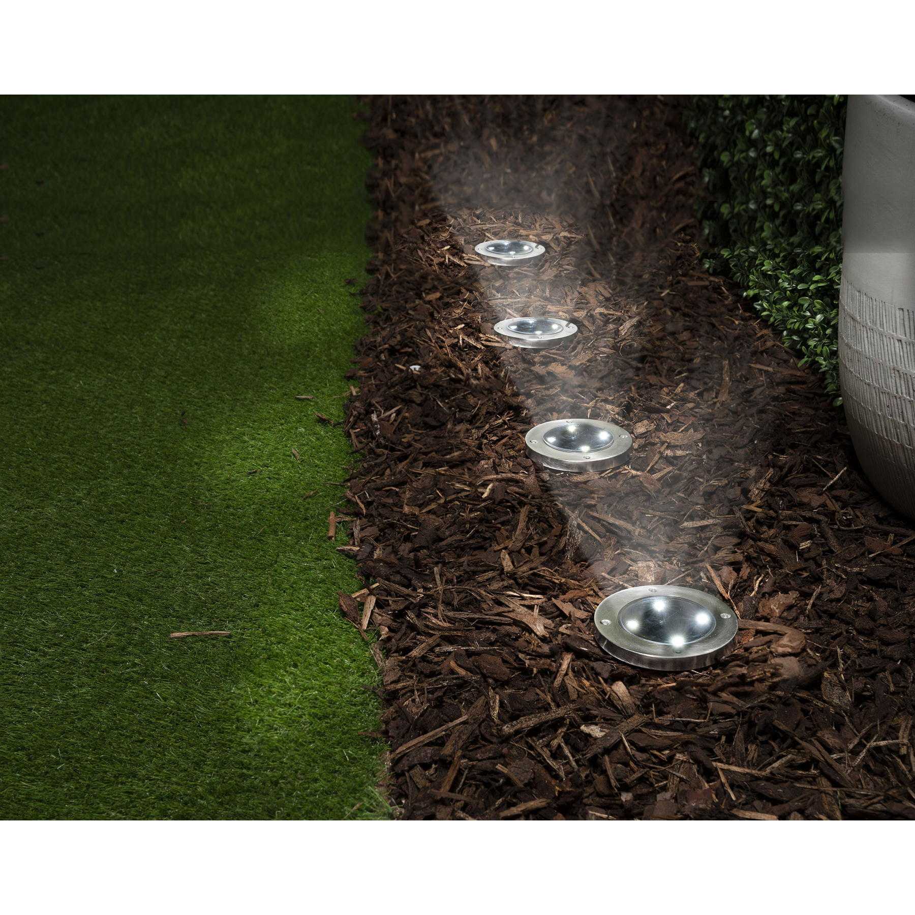 Ground lights illuminate a bark mulch path next to artificial grass.