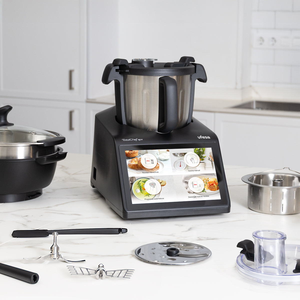 Robot de cocina negro con pantalla táctil, accesorios al lado sobre mesa de mármol.