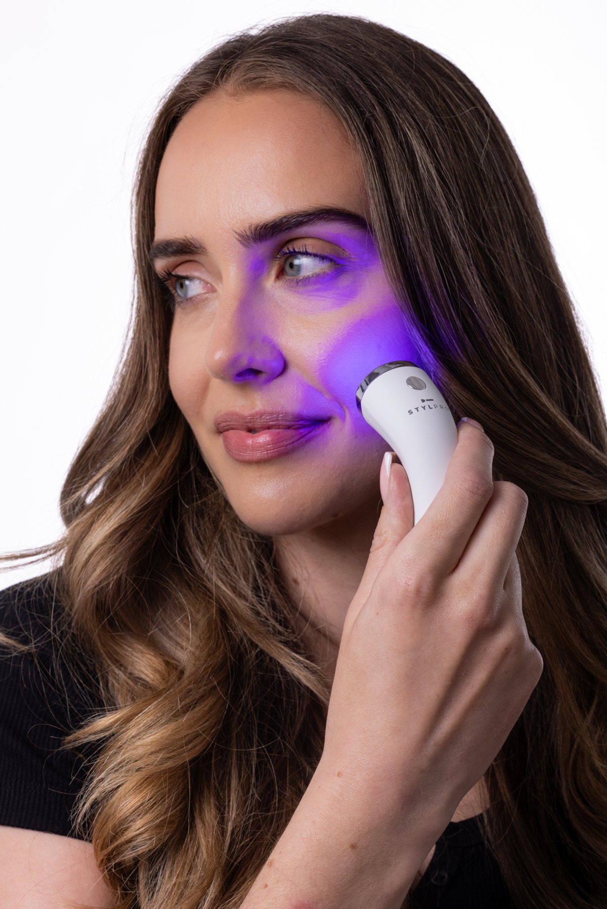 Una donna usa un dispositivo per la cura della pelle bianco con luce blu sul viso.