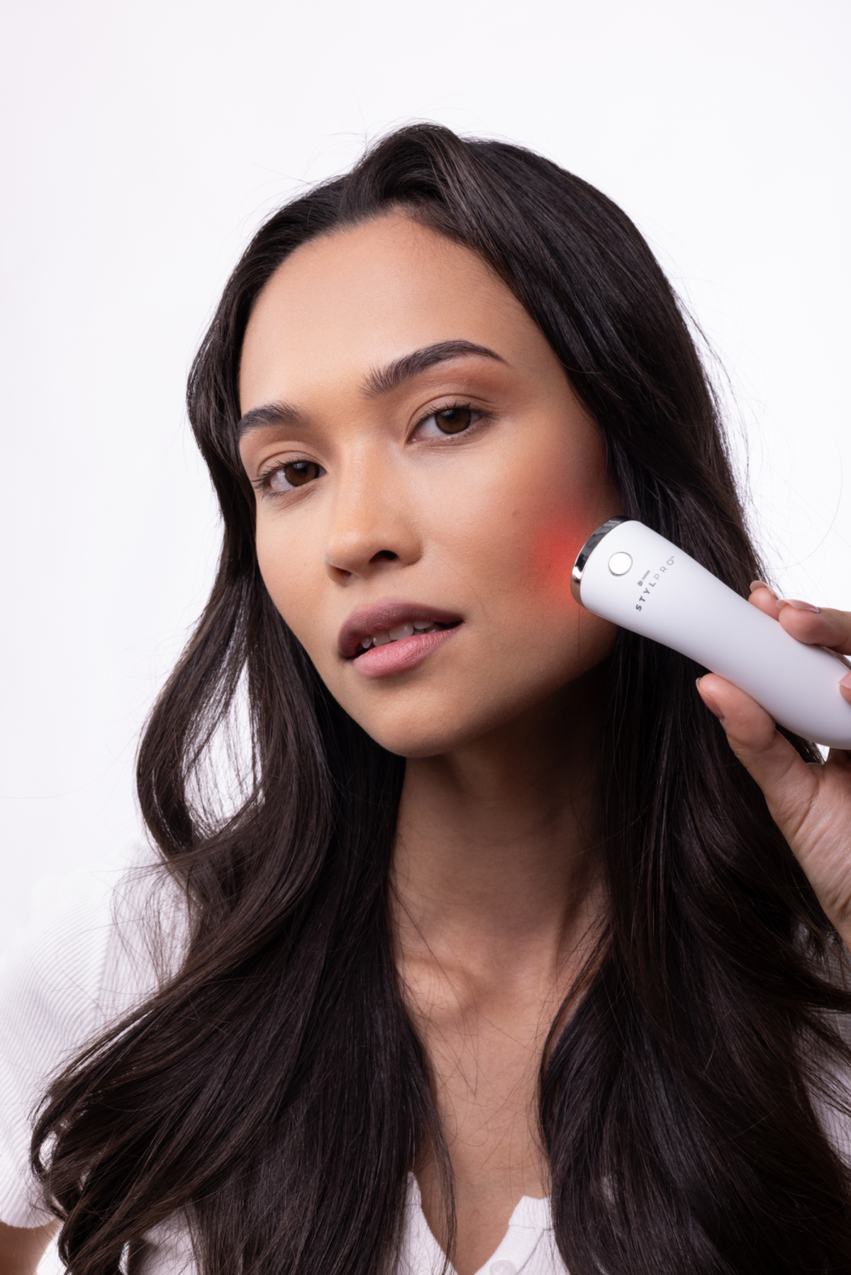 Una donna usa un dispositivo per la cura della pelle bianco con luce rossa sulla guancia.
