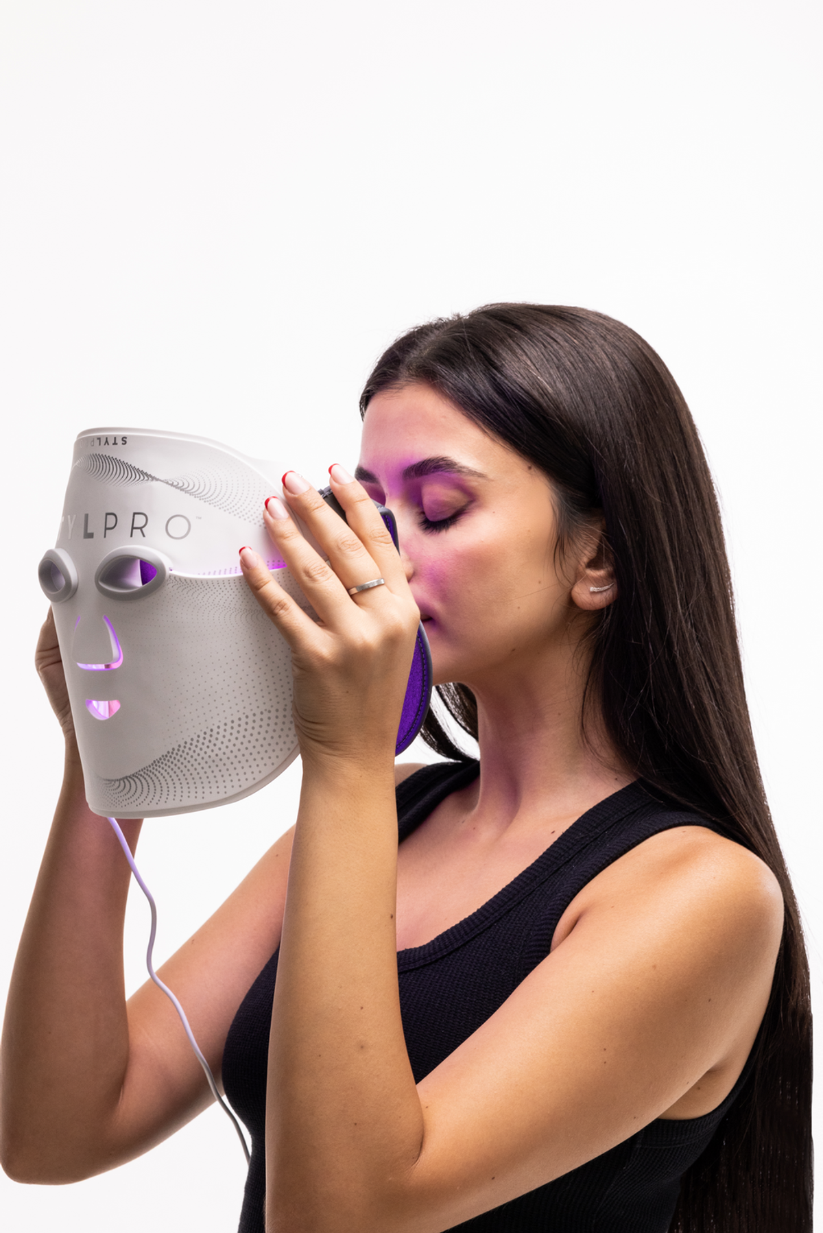 Una donna con lunghi capelli scuri tiene una maschera facciale bianca con luci viola.