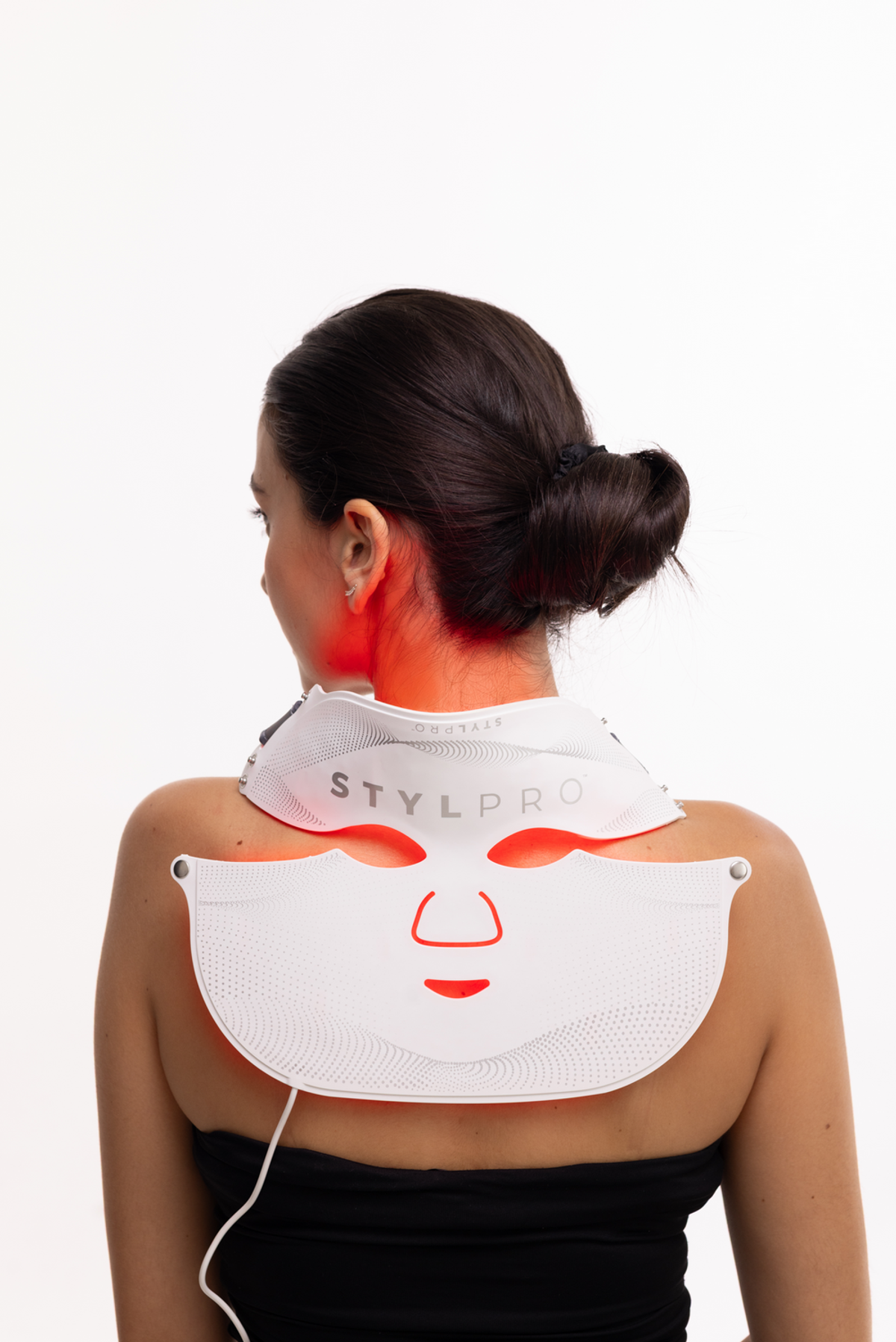 Una donna indossa una maschera facciale LED bianca con emissione di luce rossa, vista da dietro.