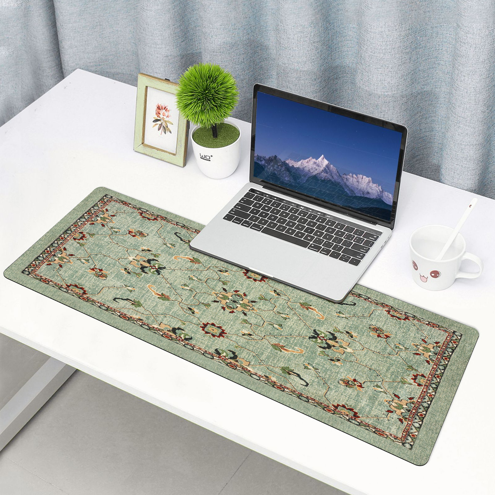 Laptop na zielonej podkładce pod biurko z motywem kwiatowym obok doniczki z rośliną.