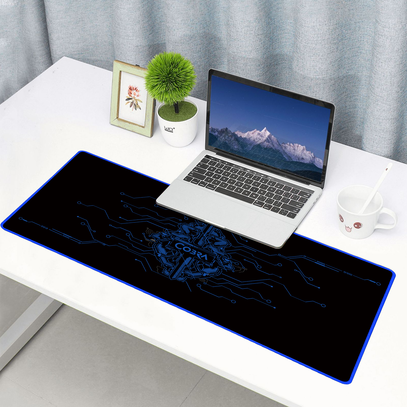 Laptop na biurku z podświetlaną podkładką pod mysz i małą rośliną.