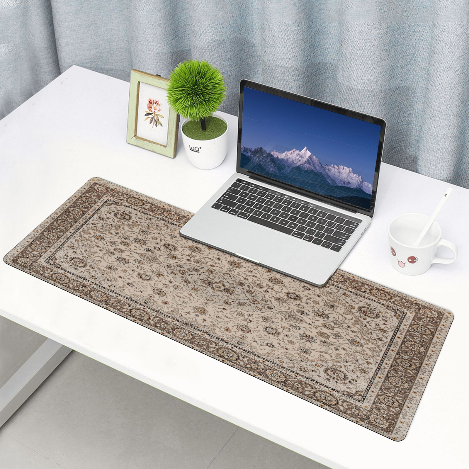 Laptop stoi na biurku z wzorzystą podkładką. Mała roślina i ramka na zdjęcie.