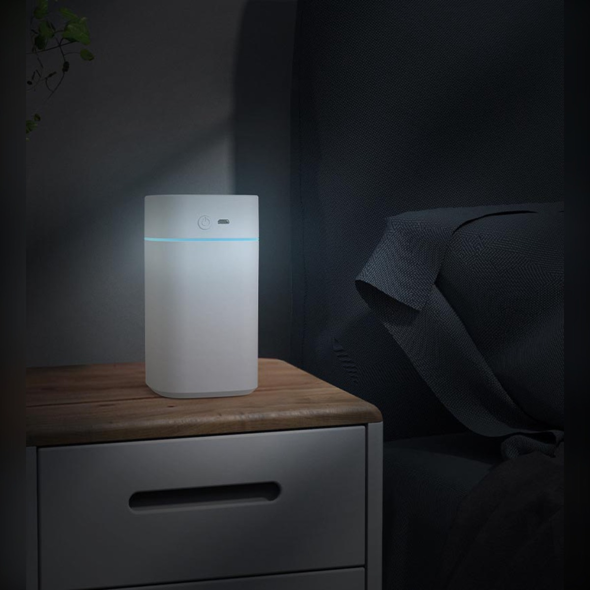 Biały nawilżacz z niebieskim światłem świeci na stoliku nocnym.