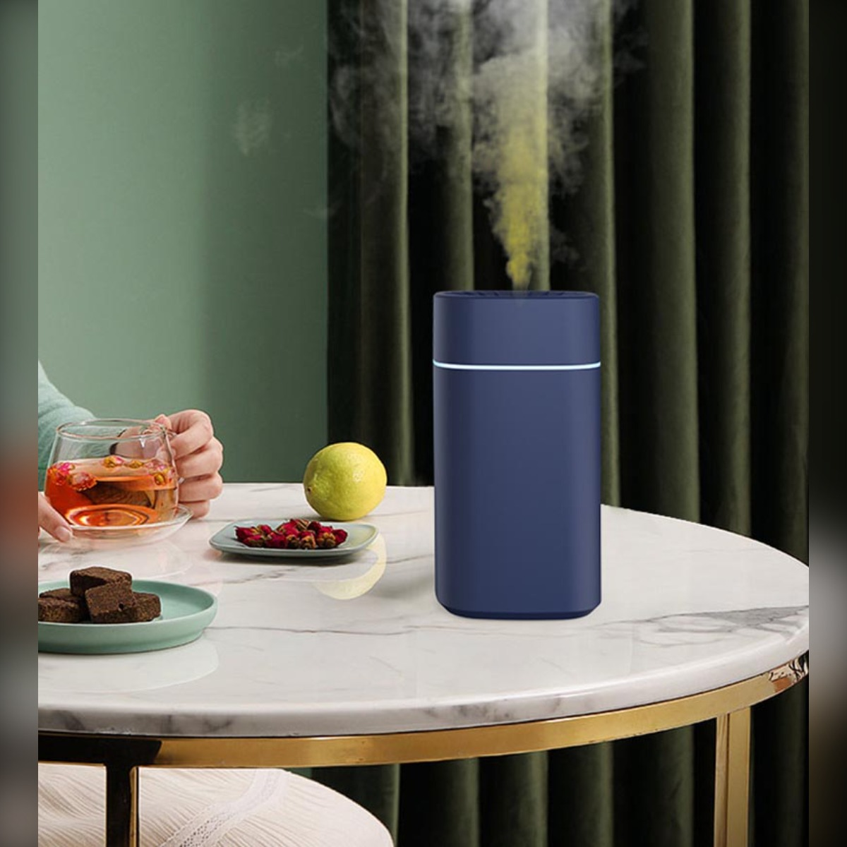 Niebieski nawilżacz emituje parę na marmurowym stole z herbatą, cytryną, przekąskami.