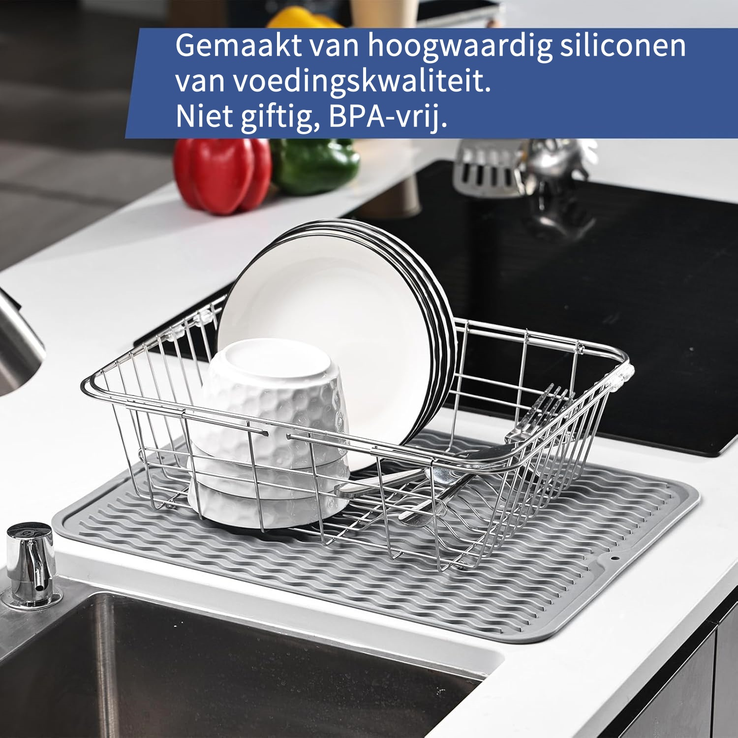 Ein Geschirrkorb aus Metall steht auf einer grauen Abtropfmatte neben einer Spüle.