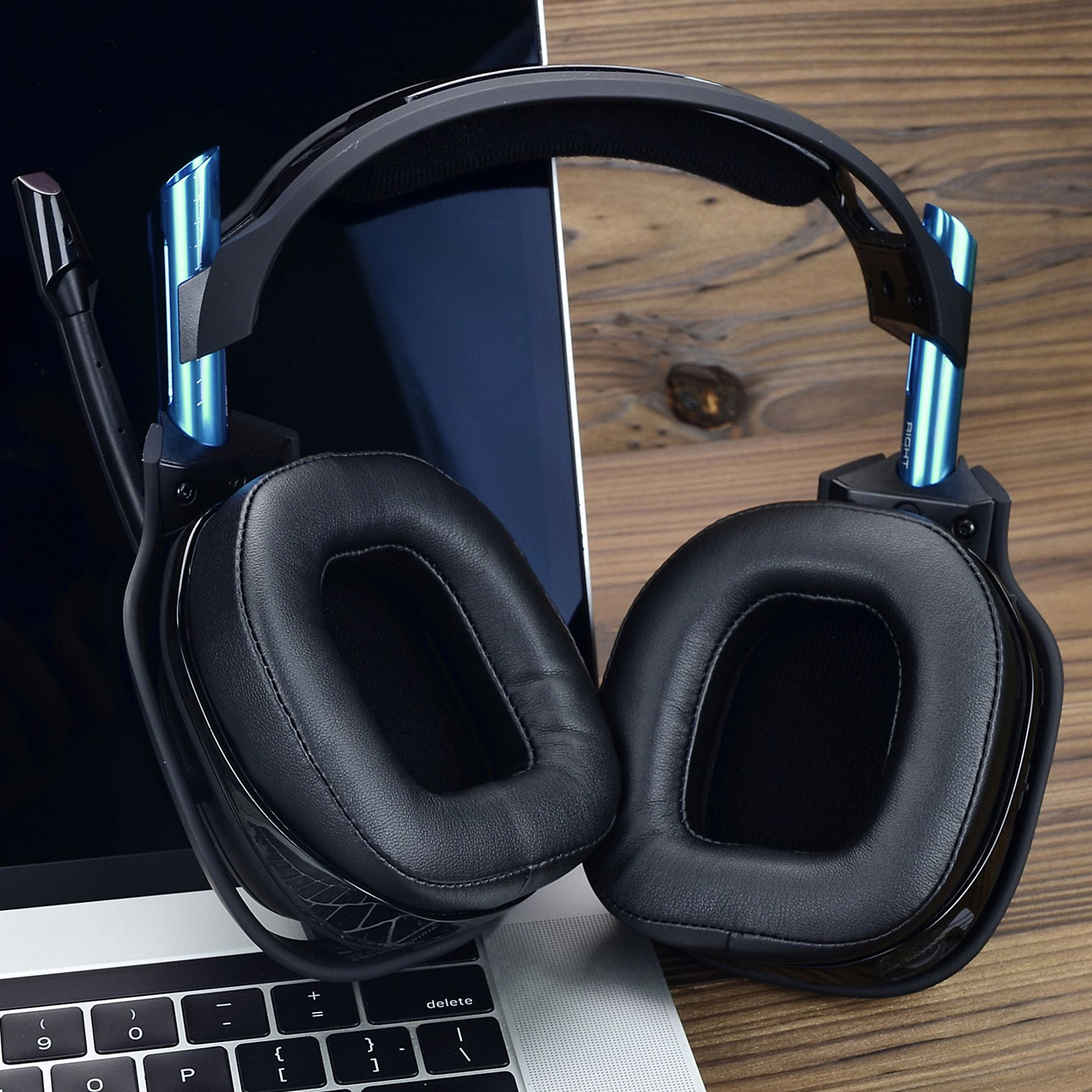 Schwarze Kopfhörer mit blauen Akzenten auf einem Laptop und Holztisch.