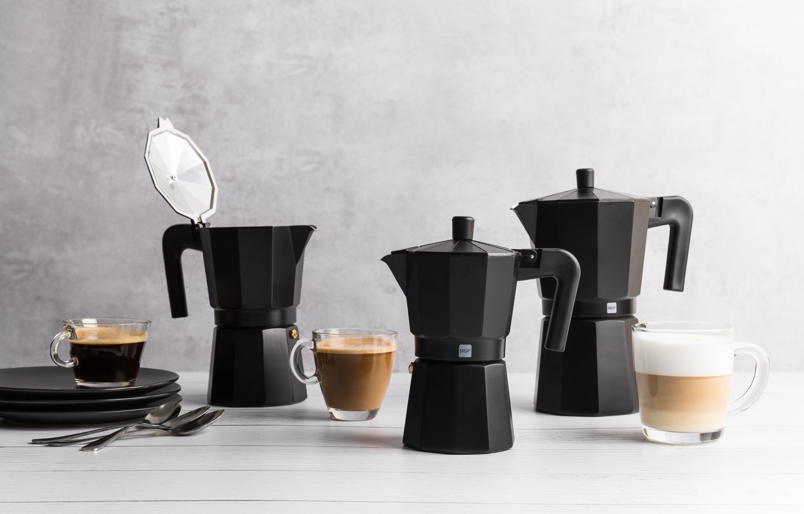 Tres cafeteras moka negras con tazas de café sobre mesa de madera.
