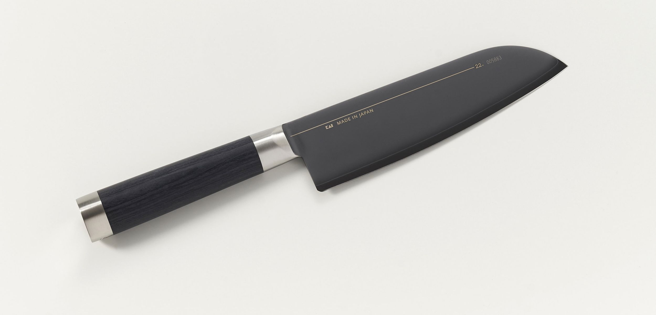 Ein schwarzes Kochmesser mit silbernem Griff liegt auf weißem Untergrund.