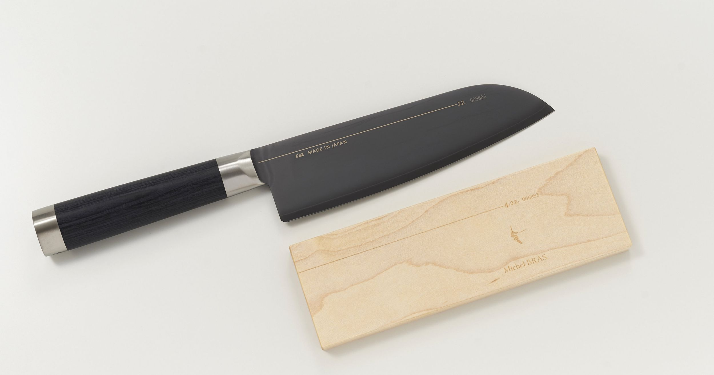 Schwarzes Messer mit Holzgriff neben einem Holzblock mit Gravur.