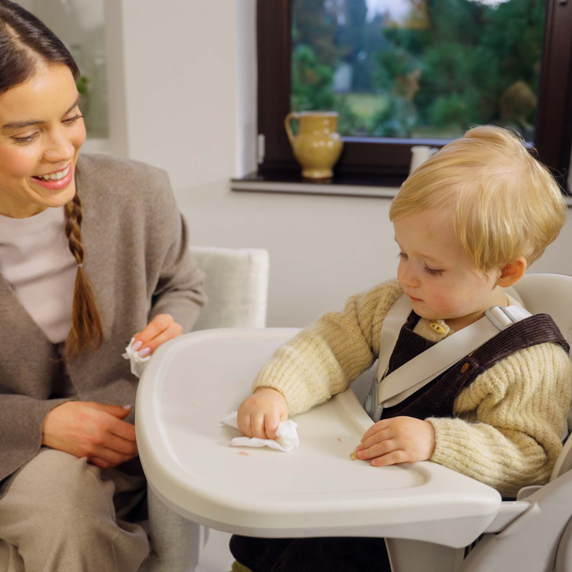 Eine Frau wischt mit einem Tuch über ein Tablett, auf dem ein Baby sitzt.