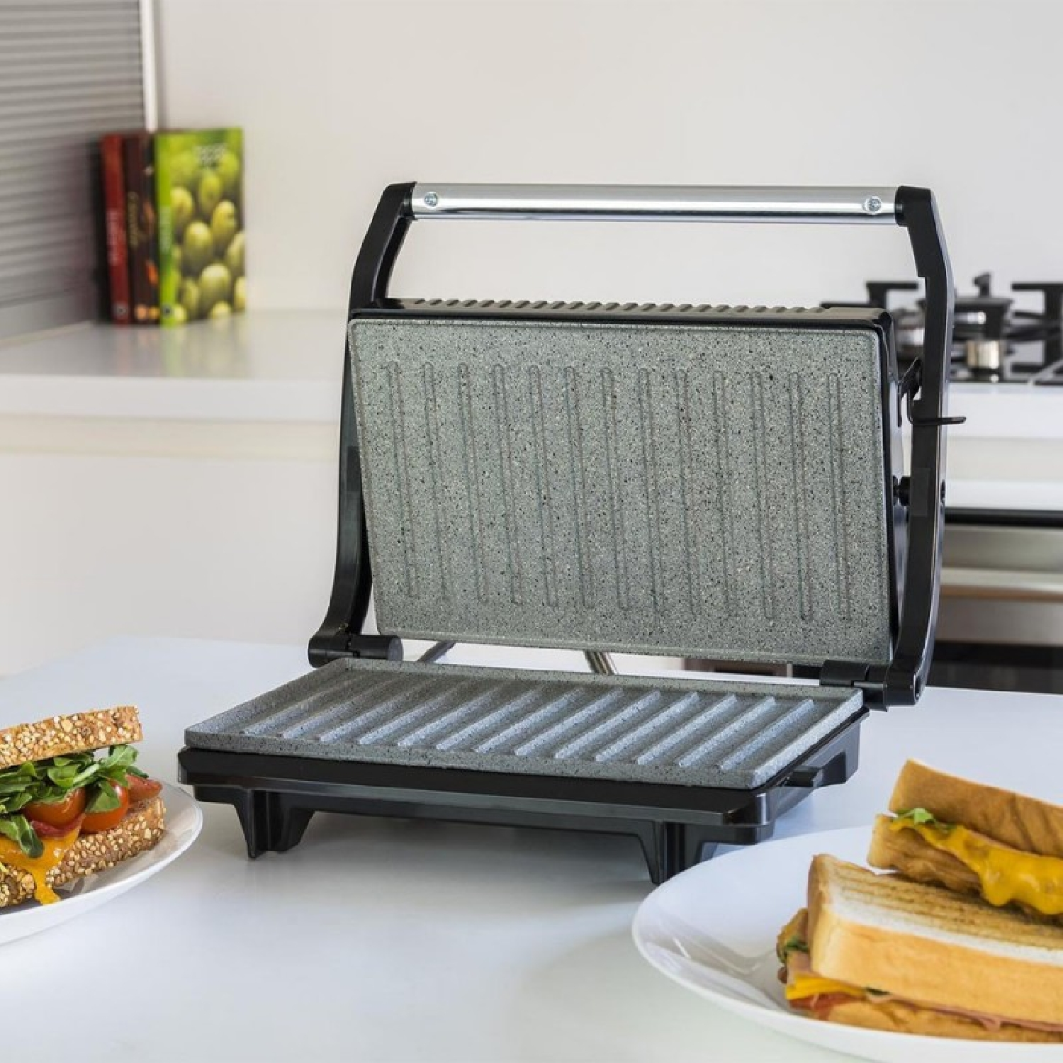 Una piastra per panini aperta con due panini su piatti davanti.