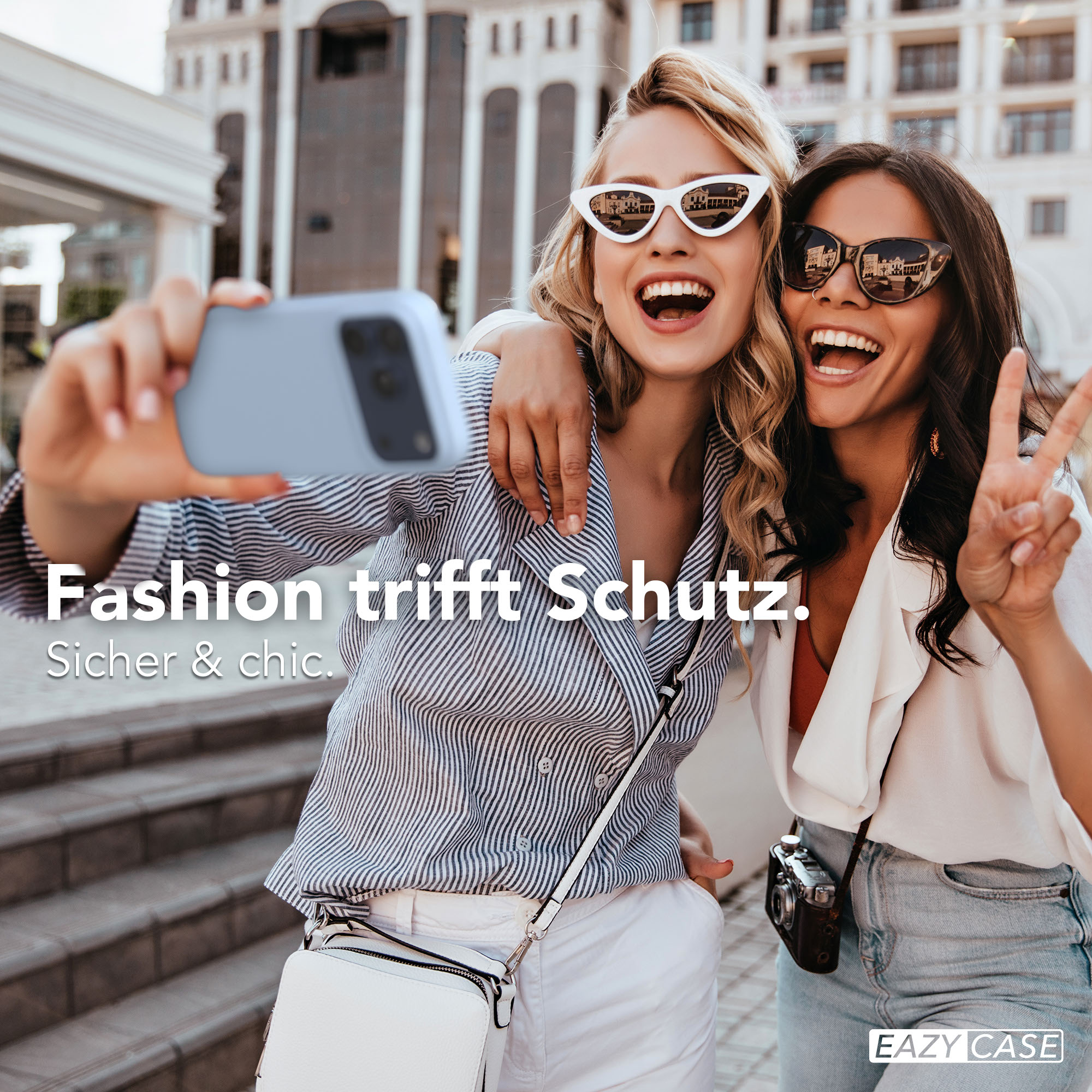 Zwei Frauen machen ein Selfie mit einem Handy in einer städtischen Umgebung.