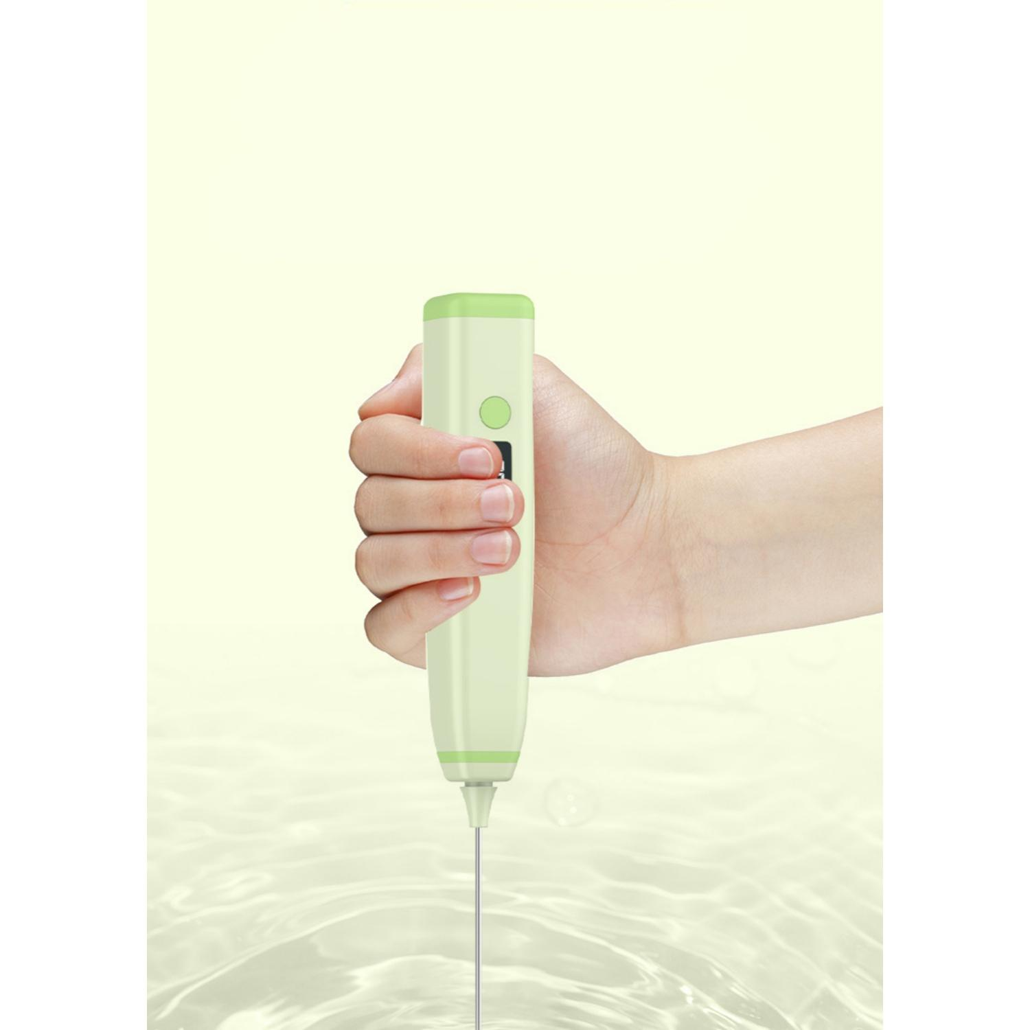 Eine Hand hält einen hellgrünen elektrischen Milchaufschäumer über leicht welligem Wasser.