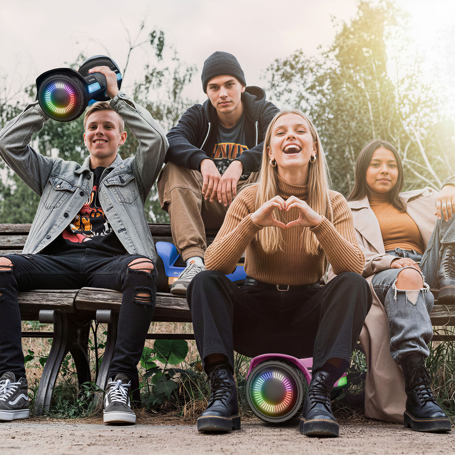 Vier junge Leute sitzen auf einer Bank mit Hoverboards. Einer hält eines hoch.