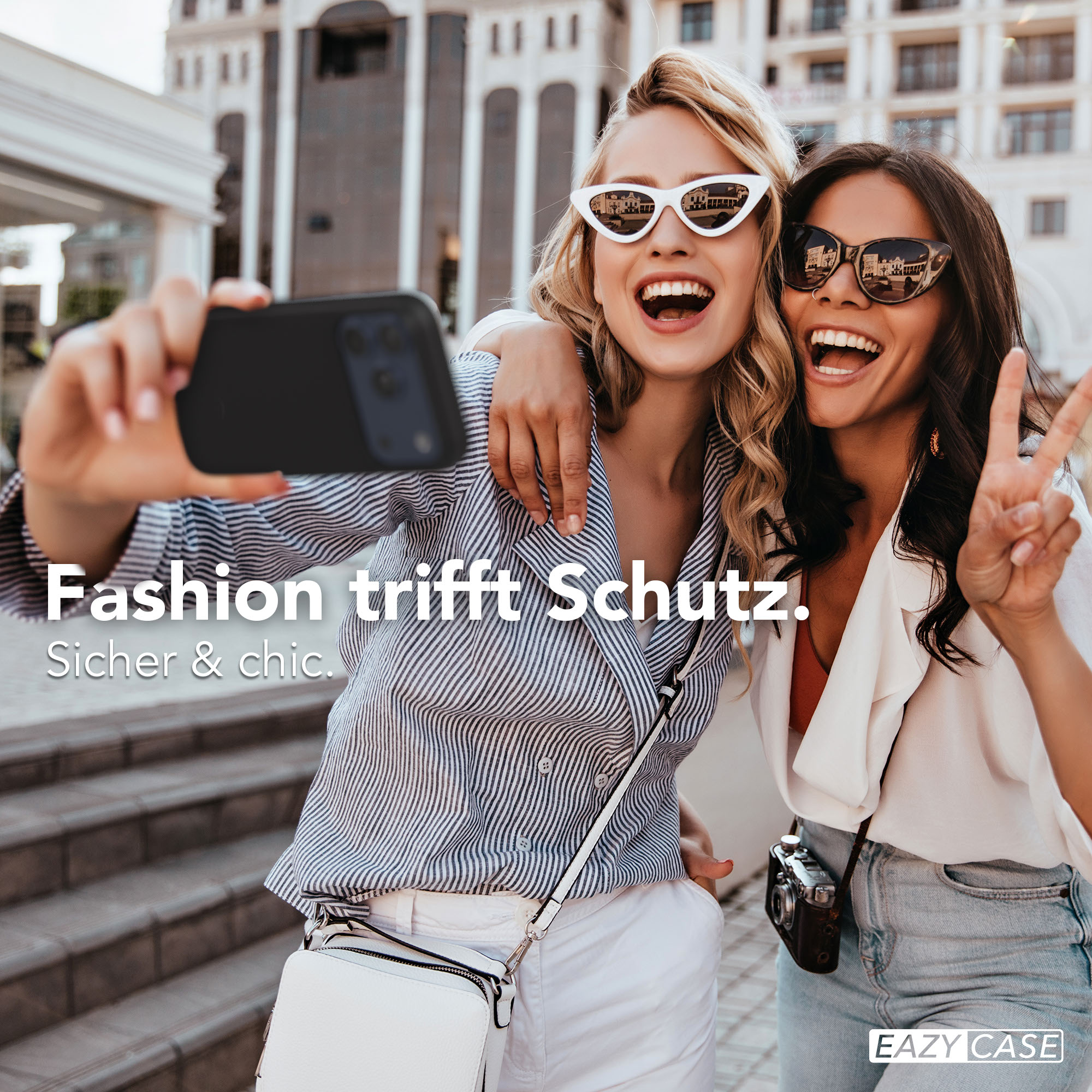Zwei Frauen machen ein Selfie vor einem Gebäude. Die eine winkt mit der Friedensgeste.