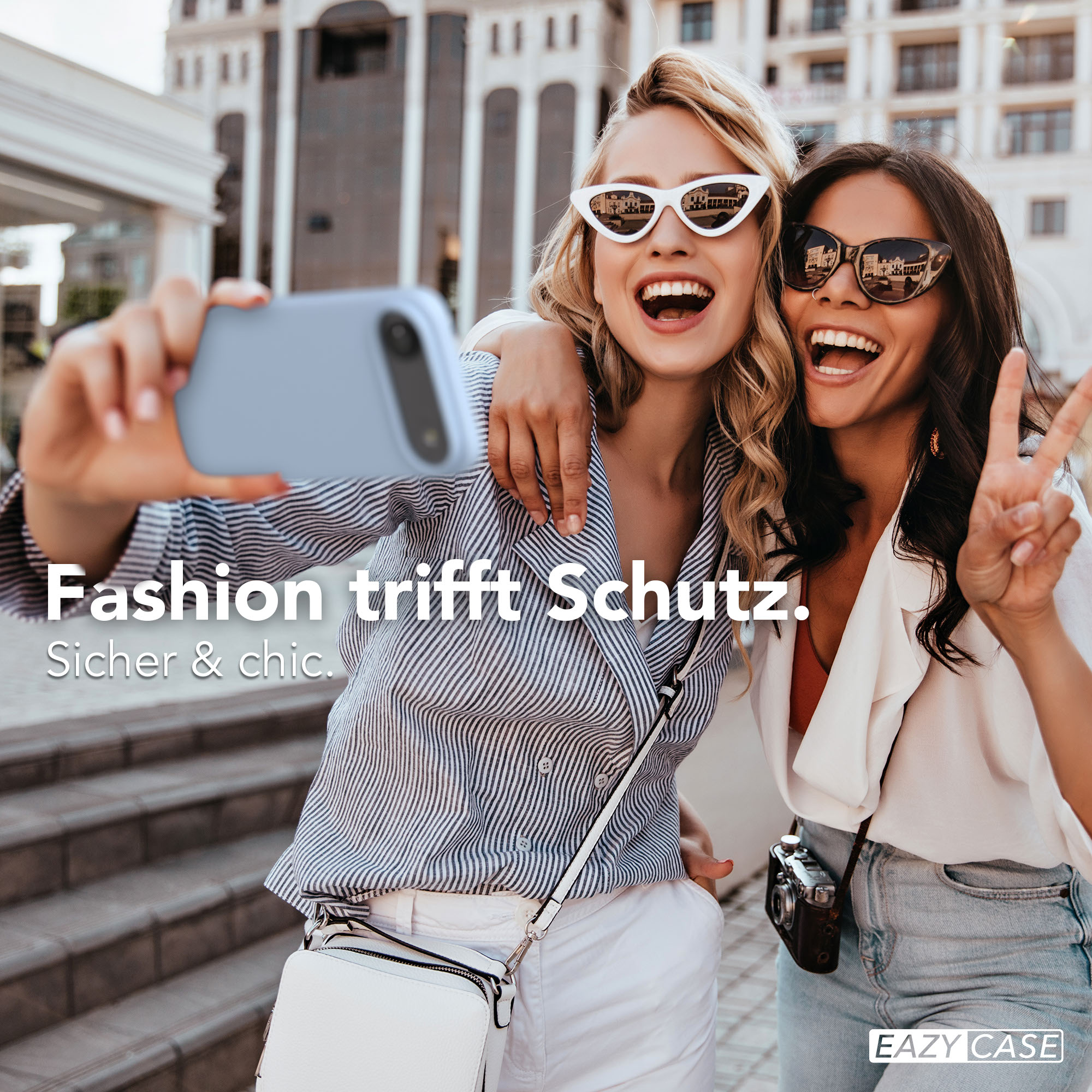 Zwei Frauen machen ein Selfie mit einem hellblauen Handy vor einem Gebäude.