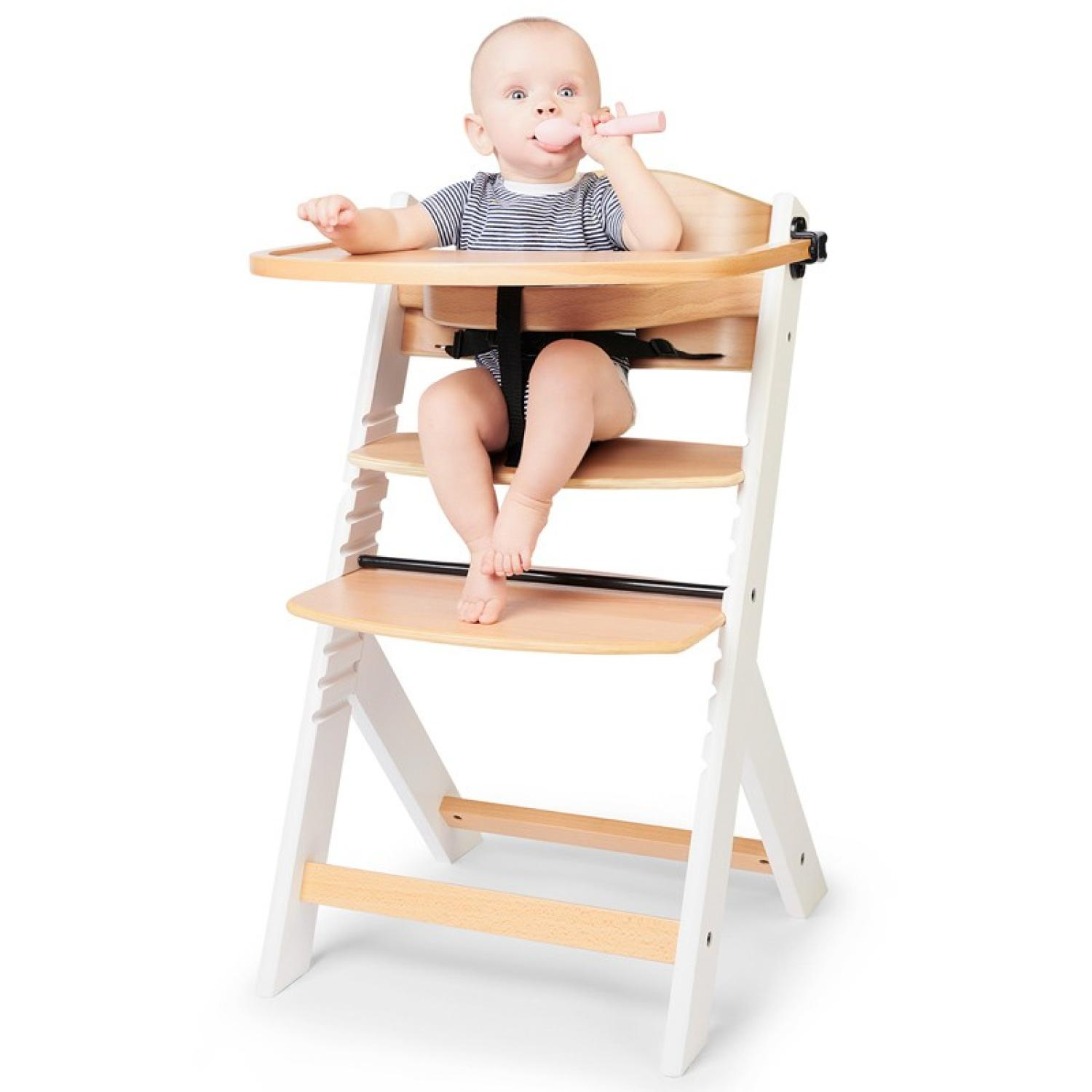 Ein Baby sitzt in einem Hochstuhl und kaut auf einem Löffel. Es trägt ein gestreiftes Oberteil.