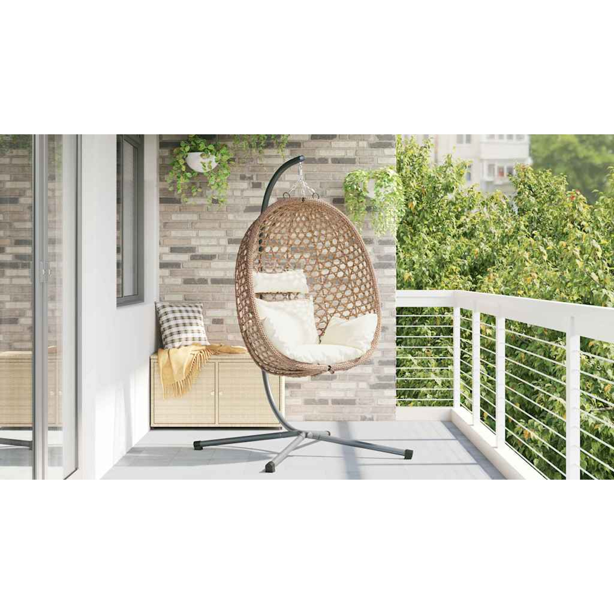 Ein Hängesessel aus Rattan mit weißen Kissen auf einer Terrasse mit Ziegelwand und Geländer.