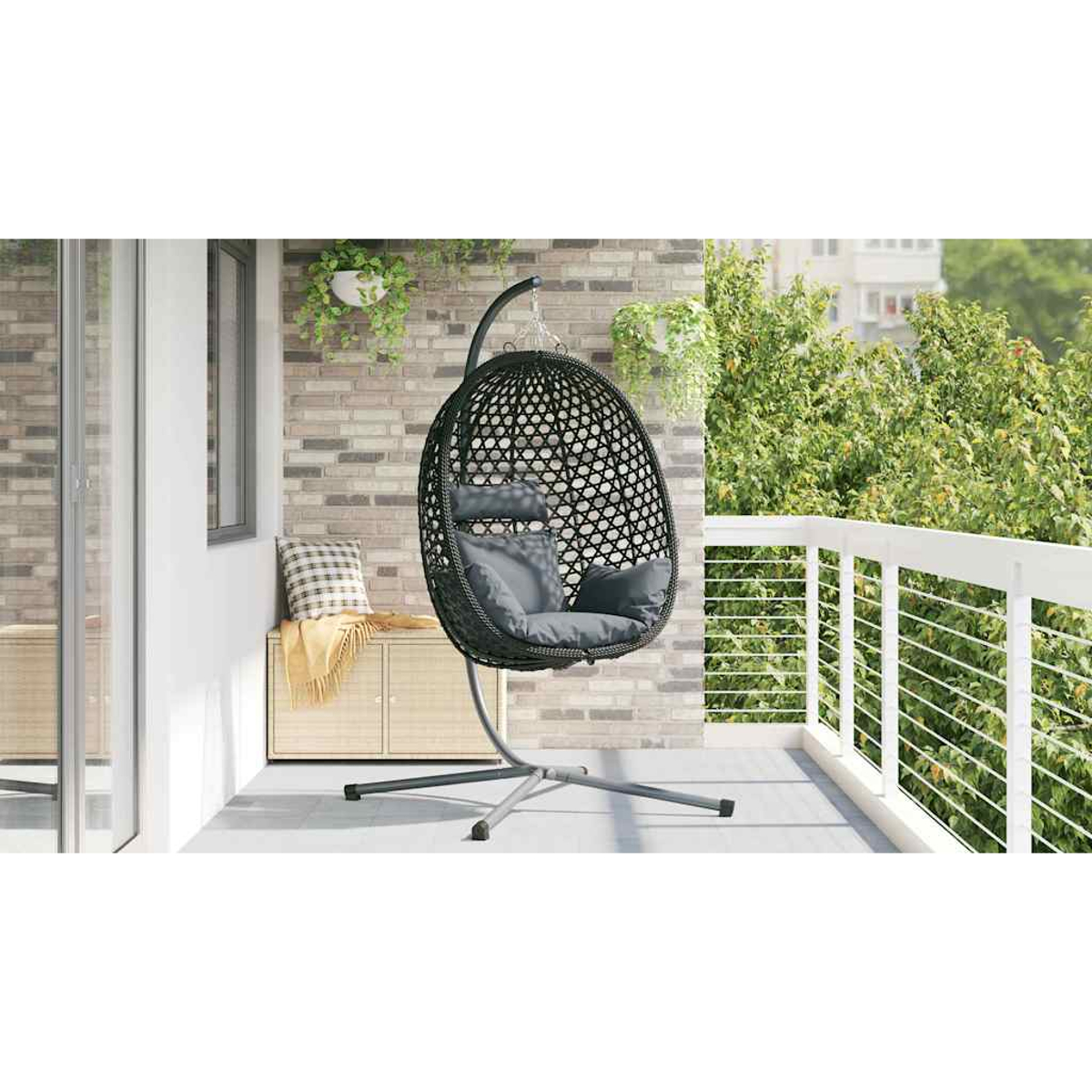 Ein dunkler Rattan-Eiersessel mit grauen Kissen steht auf einem Balkon neben einem Schrank.
