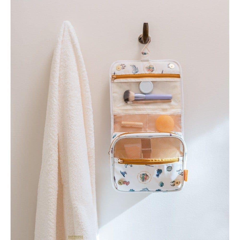 Neceser colgante con brochas de maquillaje y esponja, junto a una toalla crema.