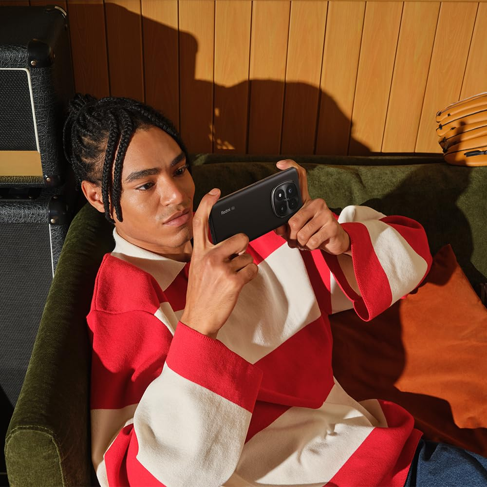 Mann in rot-weißem Pullover hält Smartphone, sitzt auf grünem Sofa.