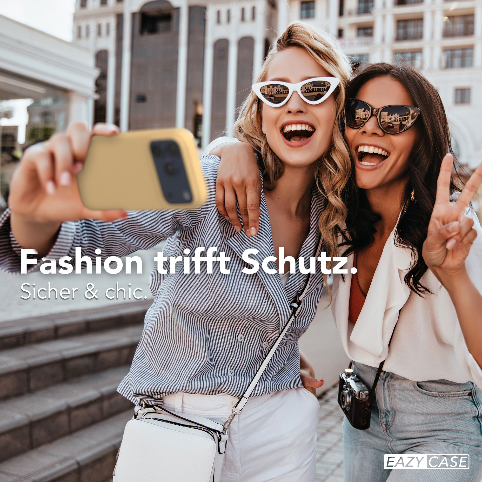 Zwei lachende Frauen machen ein Selfie mit einem Handy vor einem Gebäude.