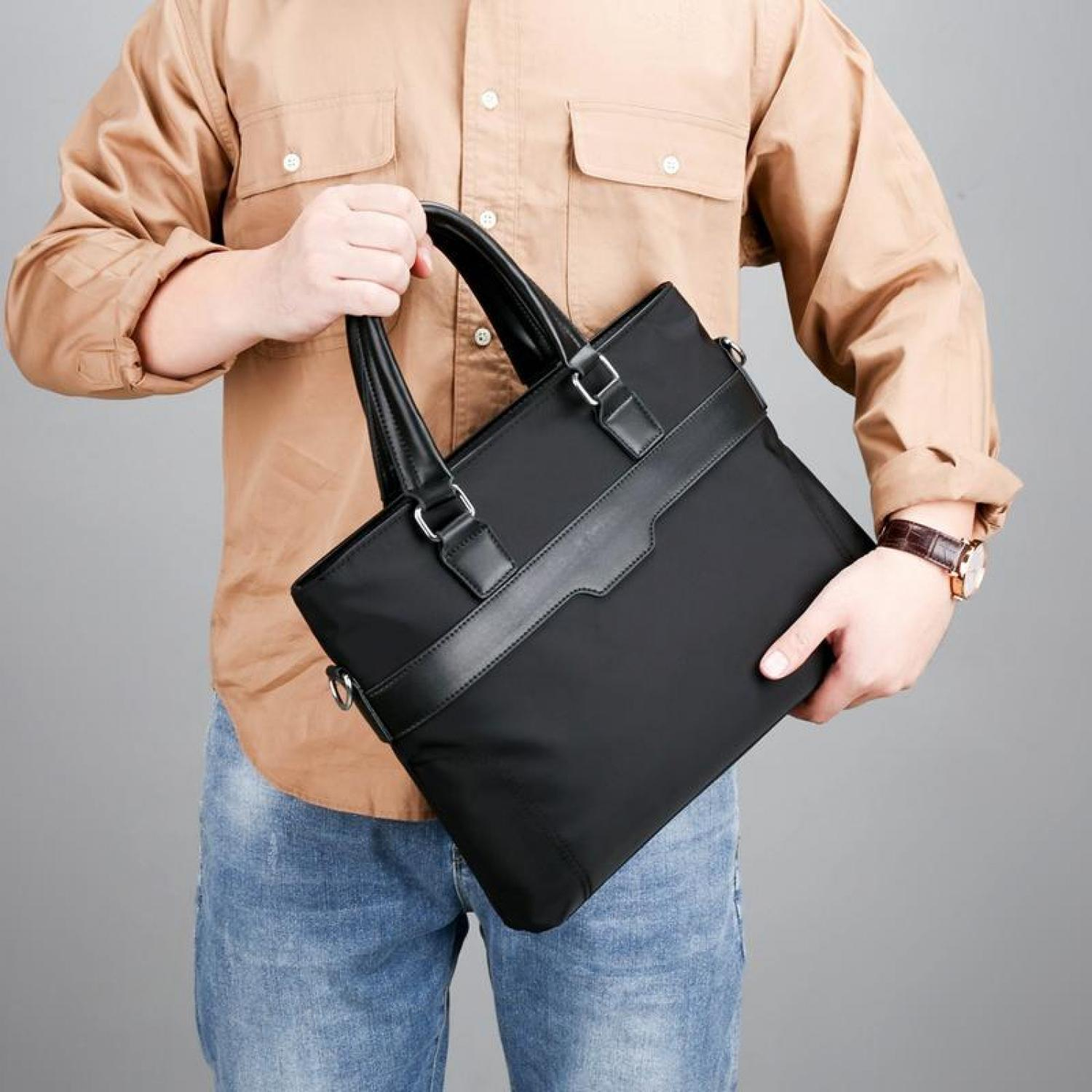 Mann in beige Hemd und Jeans hält eine schwarze Aktentasche mit Lederdetails.