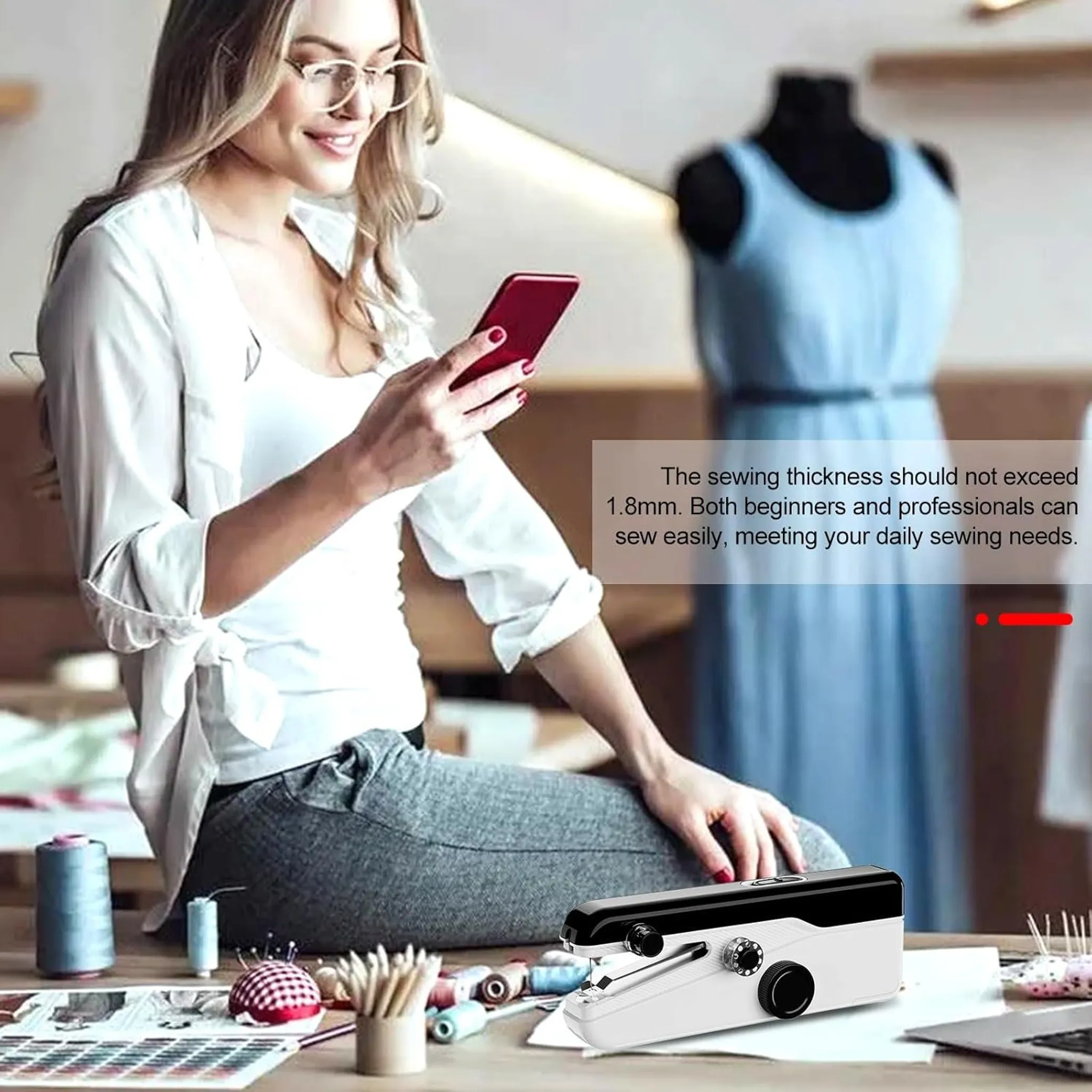 Frau mit Brille prüft Handy, Nähmaschine und Stoffe auf Tisch. Blaue Kleid-Schaufensterpuppe.