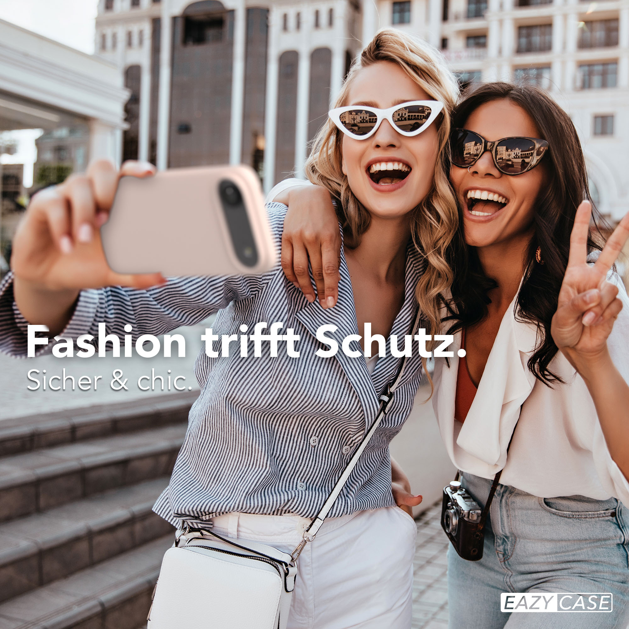 Zwei Frauen machen ein Selfie vor einem Gebäude. Eine hält ein Handy.