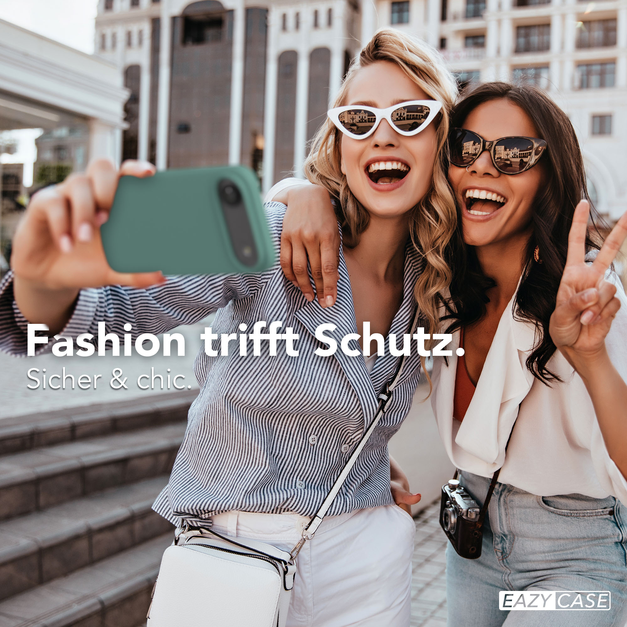 Zwei Frauen machen ein Selfie mit einem grünen Handy vor einer modernen Architektur.