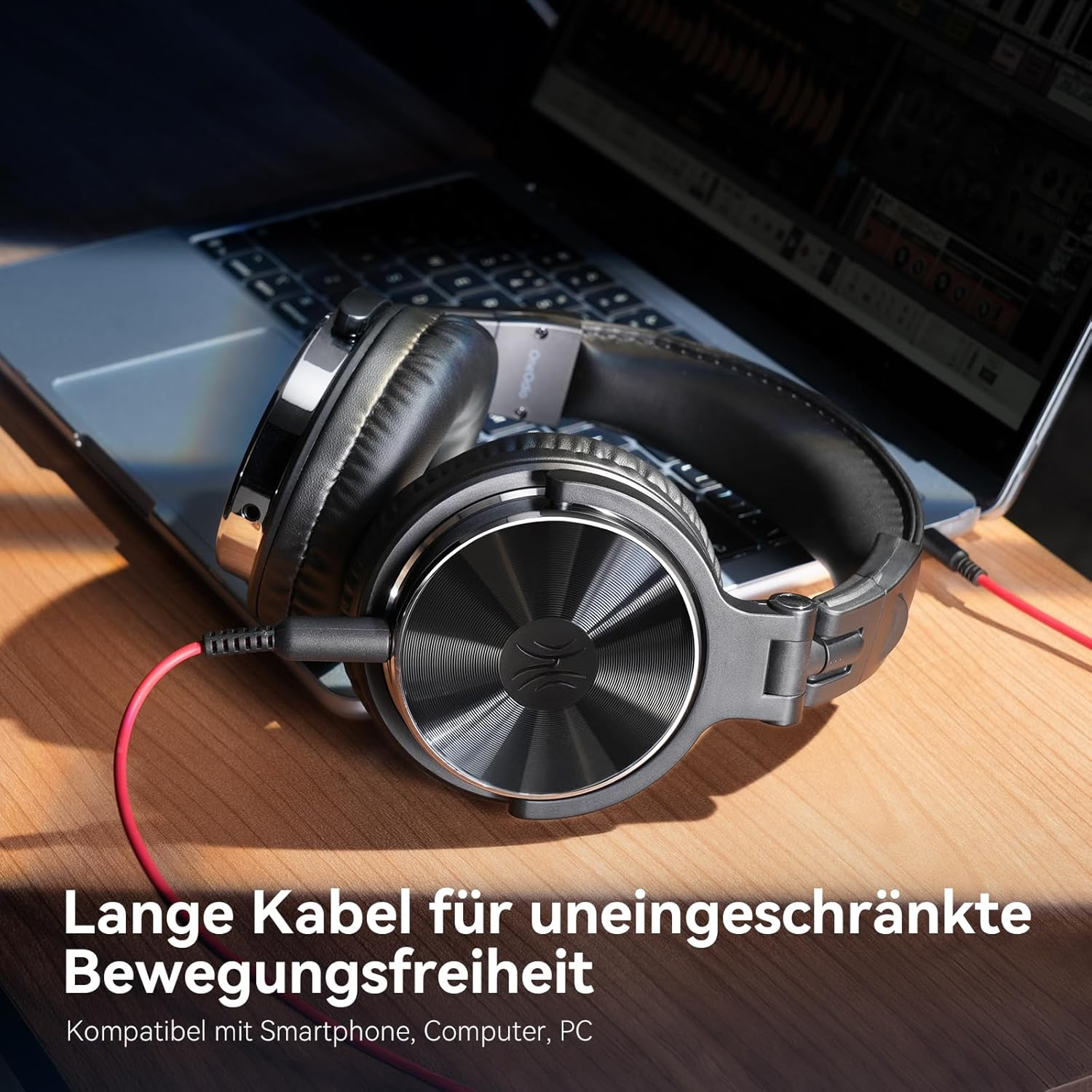 Szare słuchawki z czerwonym kablem na laptopie i drewnianym stole.