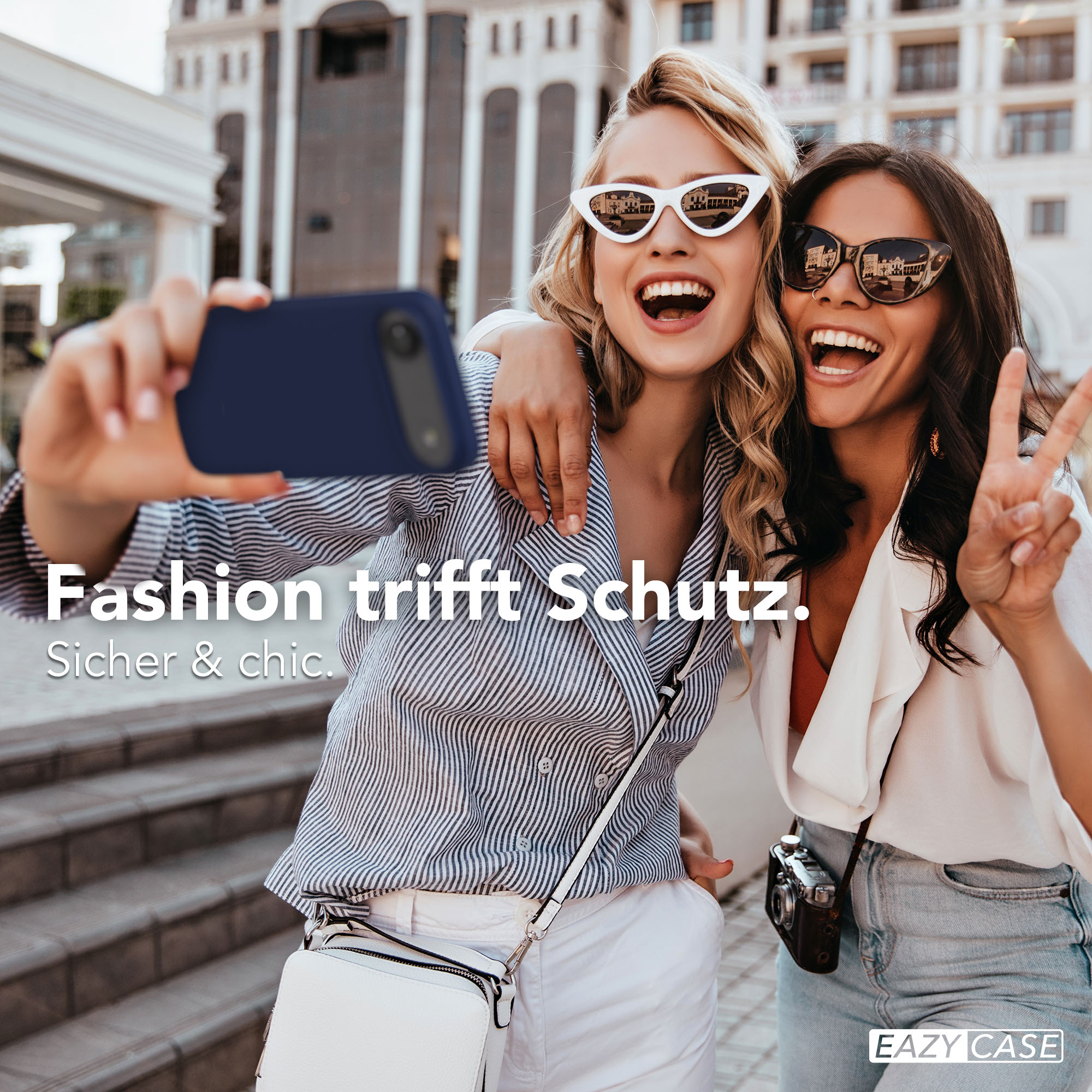 Zwei lachende Frauen machen ein Selfie mit einem Smartphone. Eine hält eine Kamera.