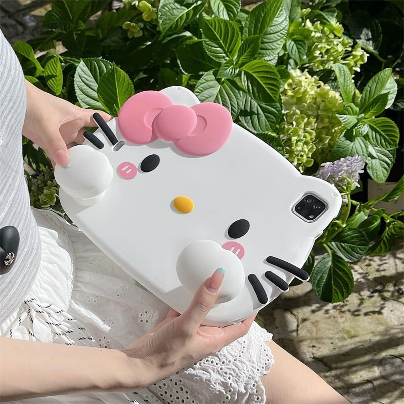 Eine Person hält eine weiße Hello Kitty Hülle mit rosa Schleife und Beeren vor Grünpflanzen.