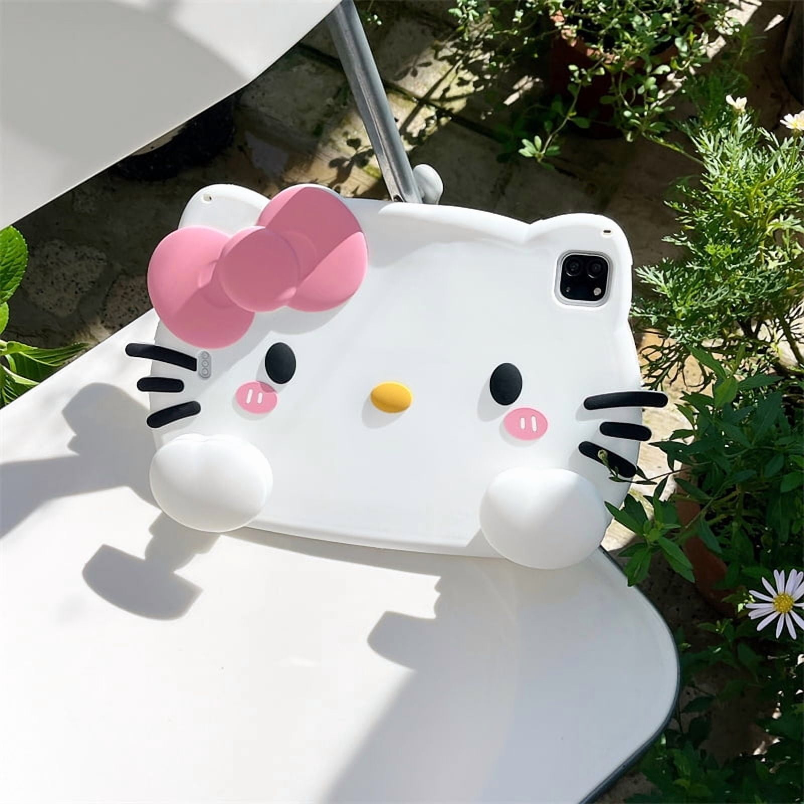 Ein weißes Hello Kitty Tablet-Case mit rosa Schleife, sitzt auf einem Tisch im Freien.