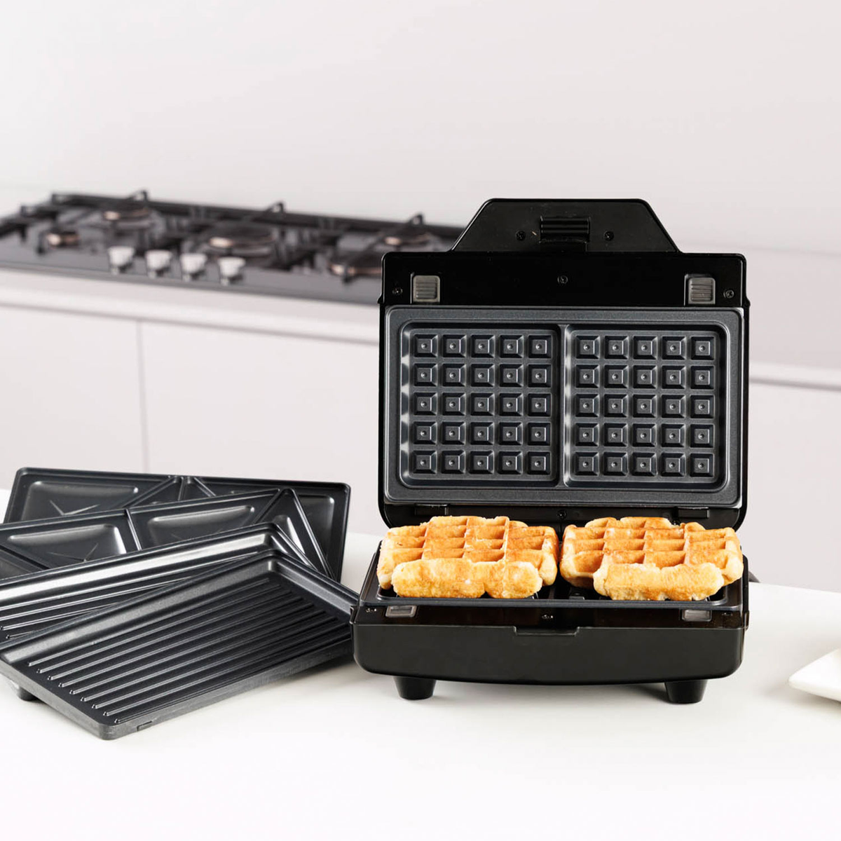 Una piastra per waffle nera aperta con due waffle dorati.