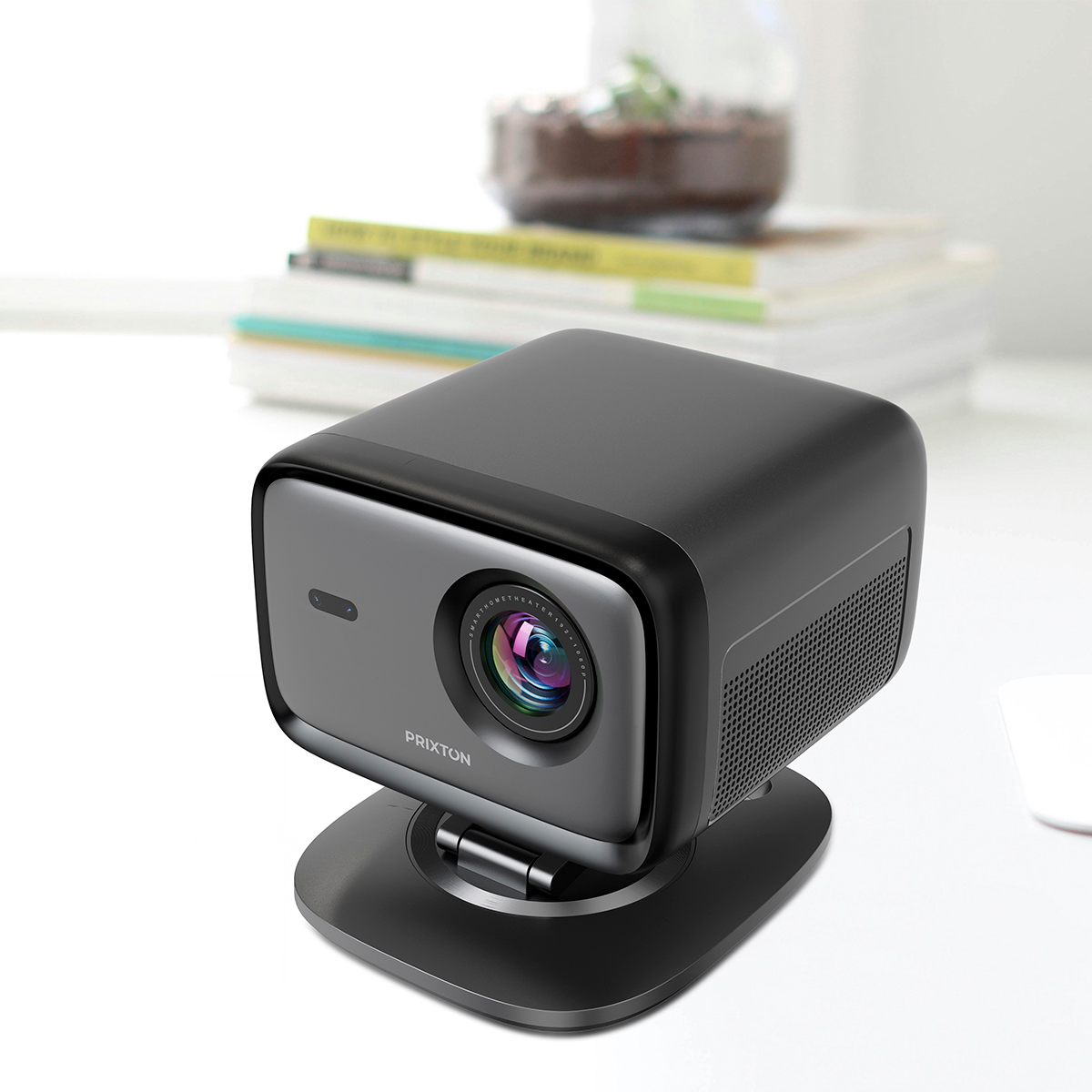 Kompaktowy, ciemny projektor stoi na podstawce przed książkami i rośliną.