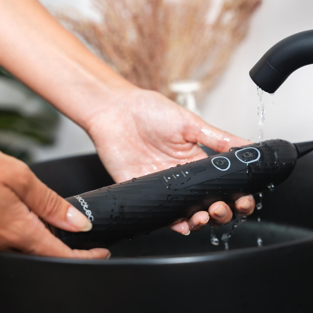 Manos enjuagando un irrigador bucal negro bajo agua corriente.