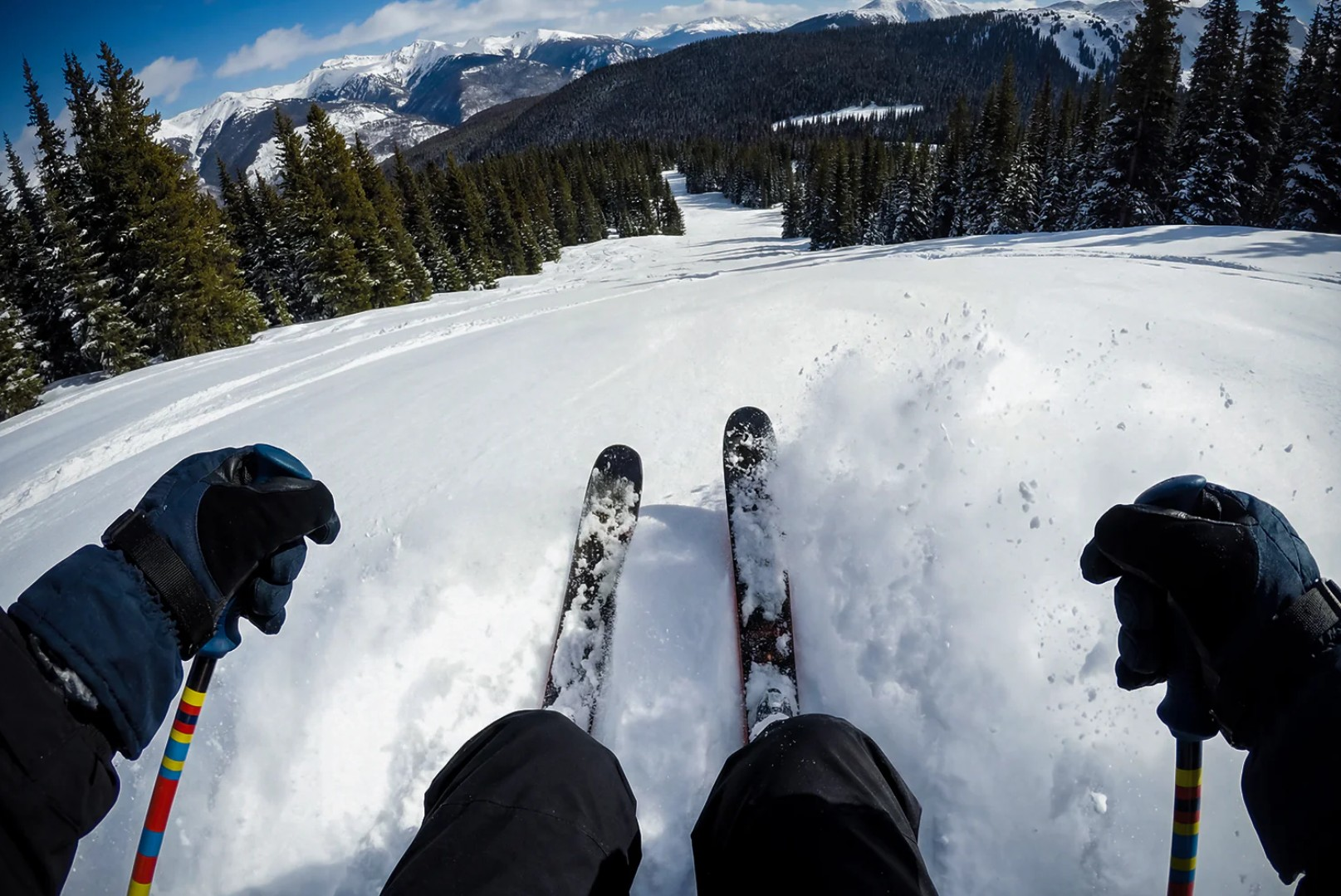 Skifahren einen verschneiten Hang hinunter mit Kiefern und Bergen im Hintergrund.